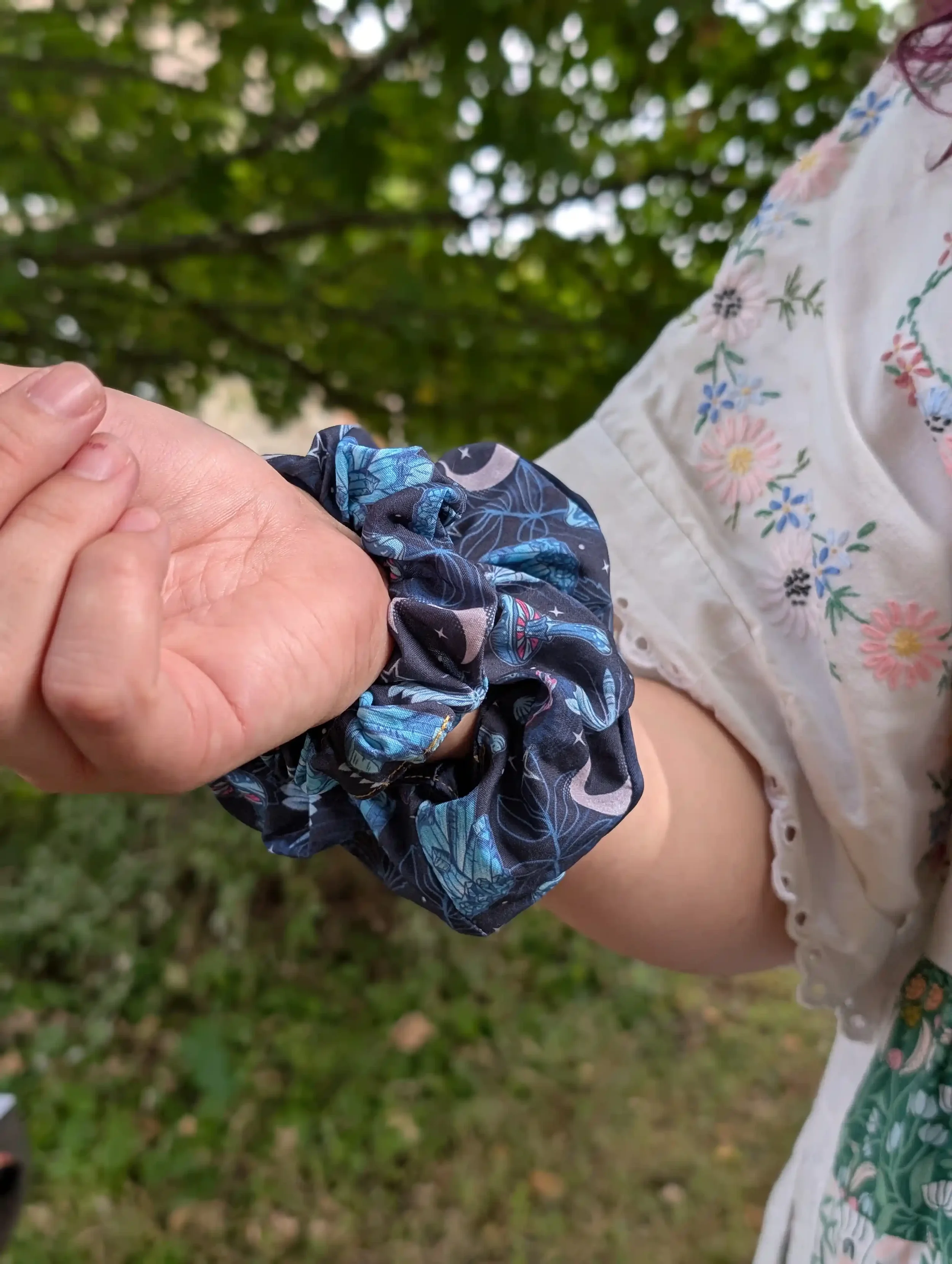 Chouchou Cristal noir et bleu à motifs célestes porté au poignet, vue rapprochée.