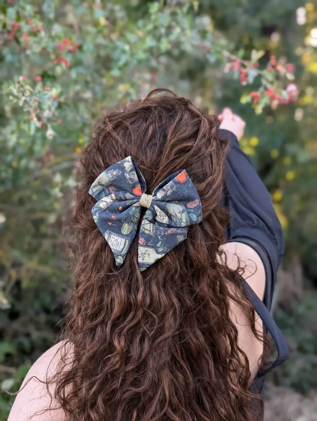 Nœud pour cheveux Alchimique à motifs de fioles et de plantes porté en demi-queue dans un jardin.