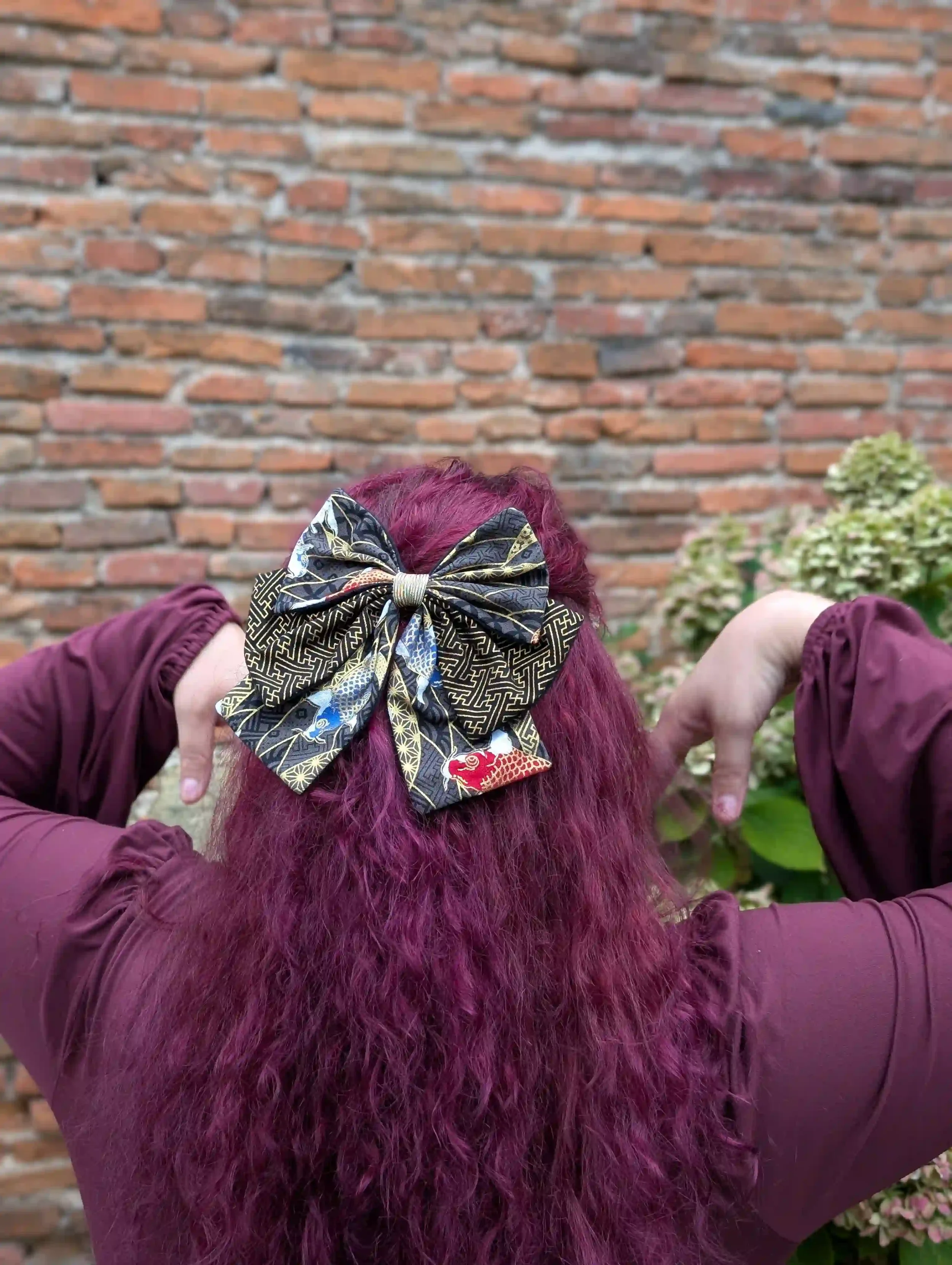 Nœud cheveux Koï noir porté en demi-queue devant un mur en briques, motif carpes japonaises dorées sur tissu Sayagata noir et or.