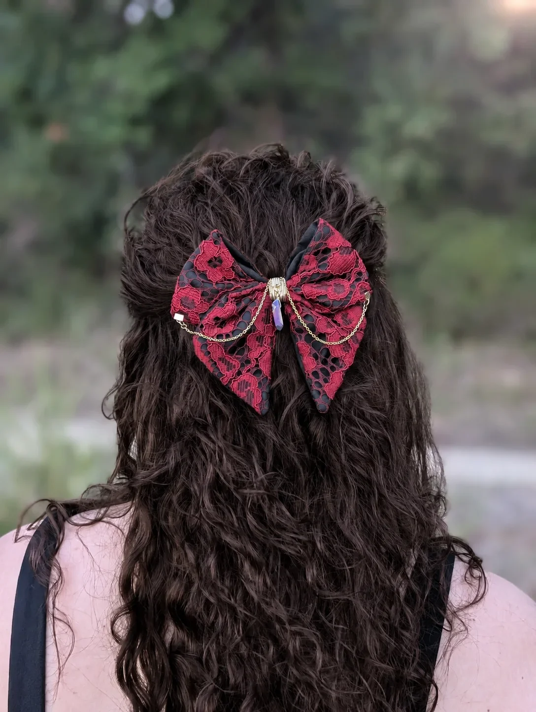Nœud bijou en dentelle rouge et noire sur cheveux bruns bouclés, porté en demi-queue.