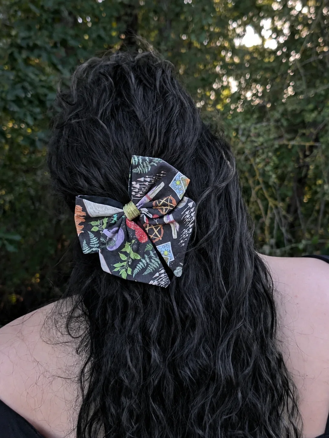 Nœud barrette à champignons, feuillages et cartes sur fond sombre, porté dans des cheveux noirs de trois quarts.