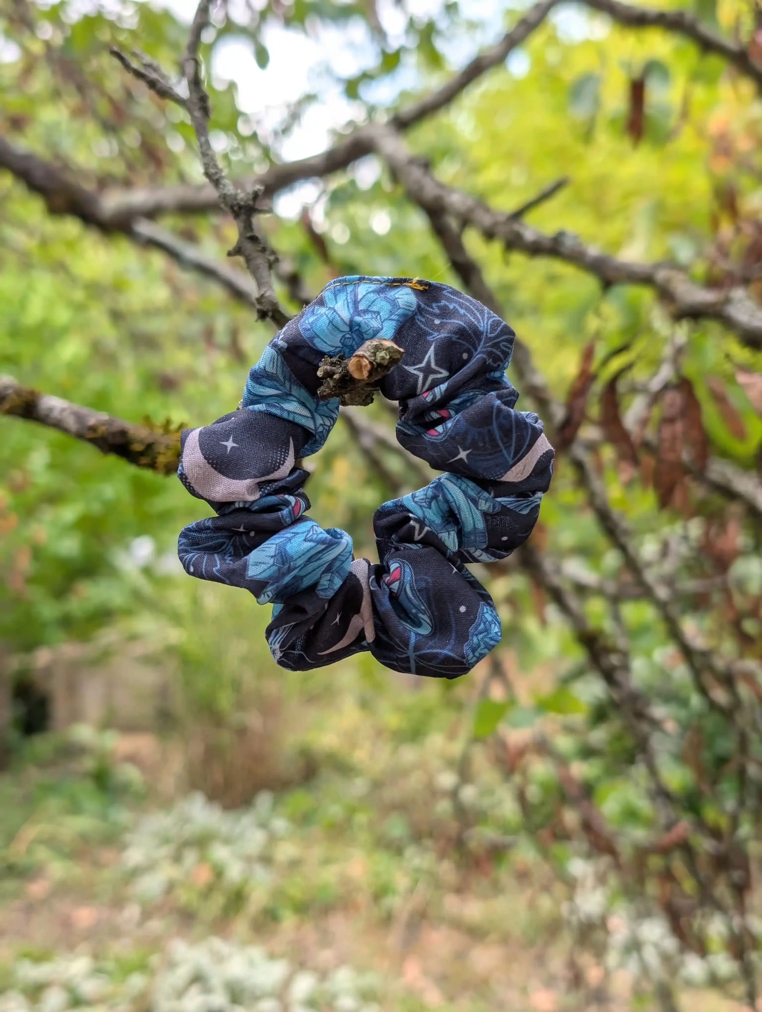 Chouchou Cristal noir et bleu à motifs de cristaux, lunes et étoiles, présenté dans un décor végétal.