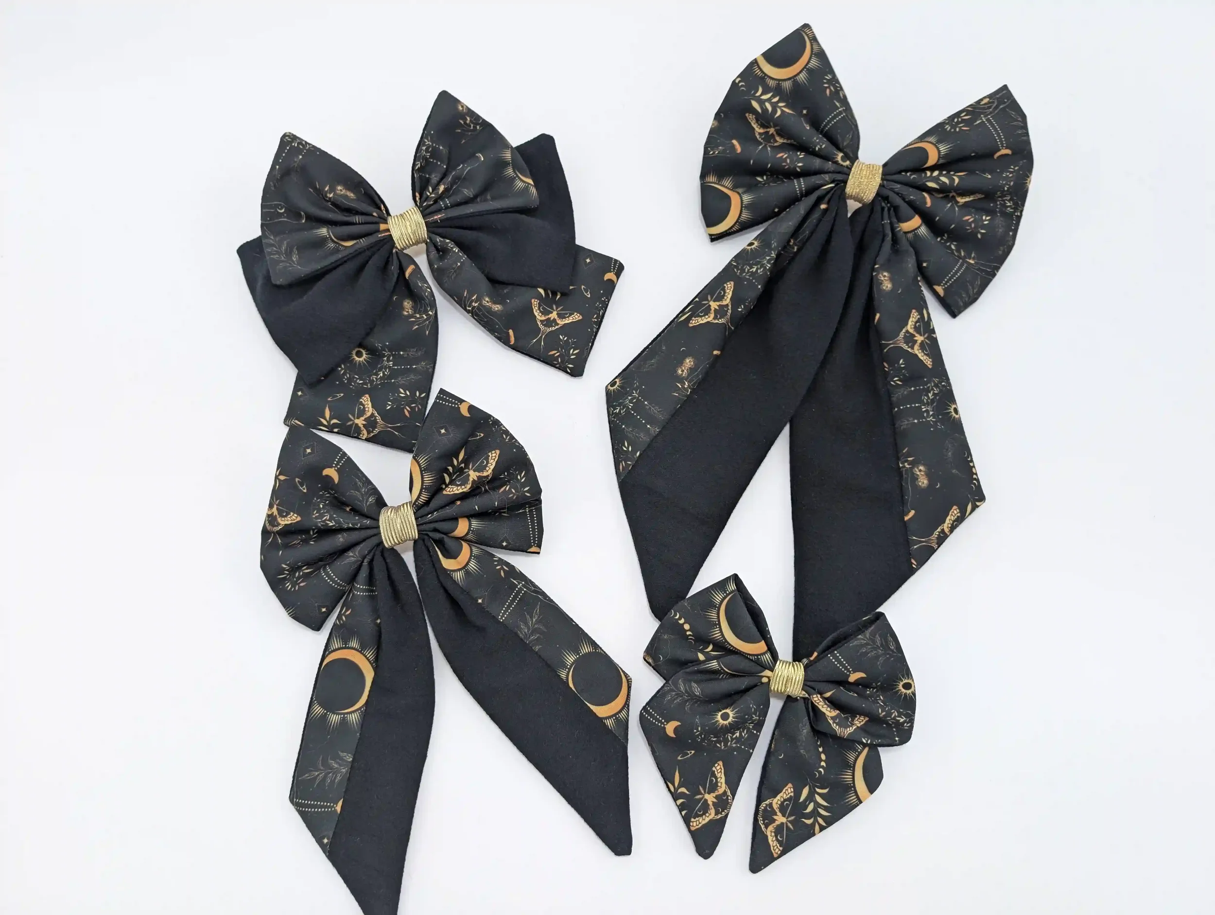 Collection des quatre tailles du nœud pour cheveux Moon, en tissu noir à motifs witchy dorés et pointes noires.