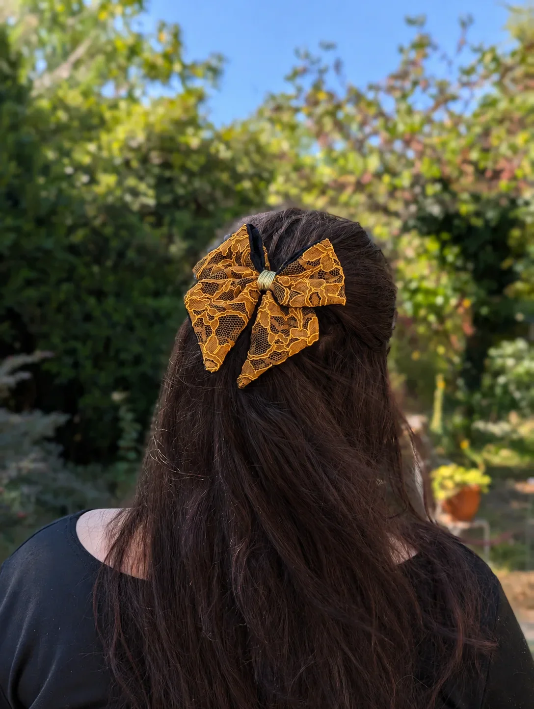 Nœud pour cheveux en dentelle ocre doré et tissu noir, porté sur cheveux longs.