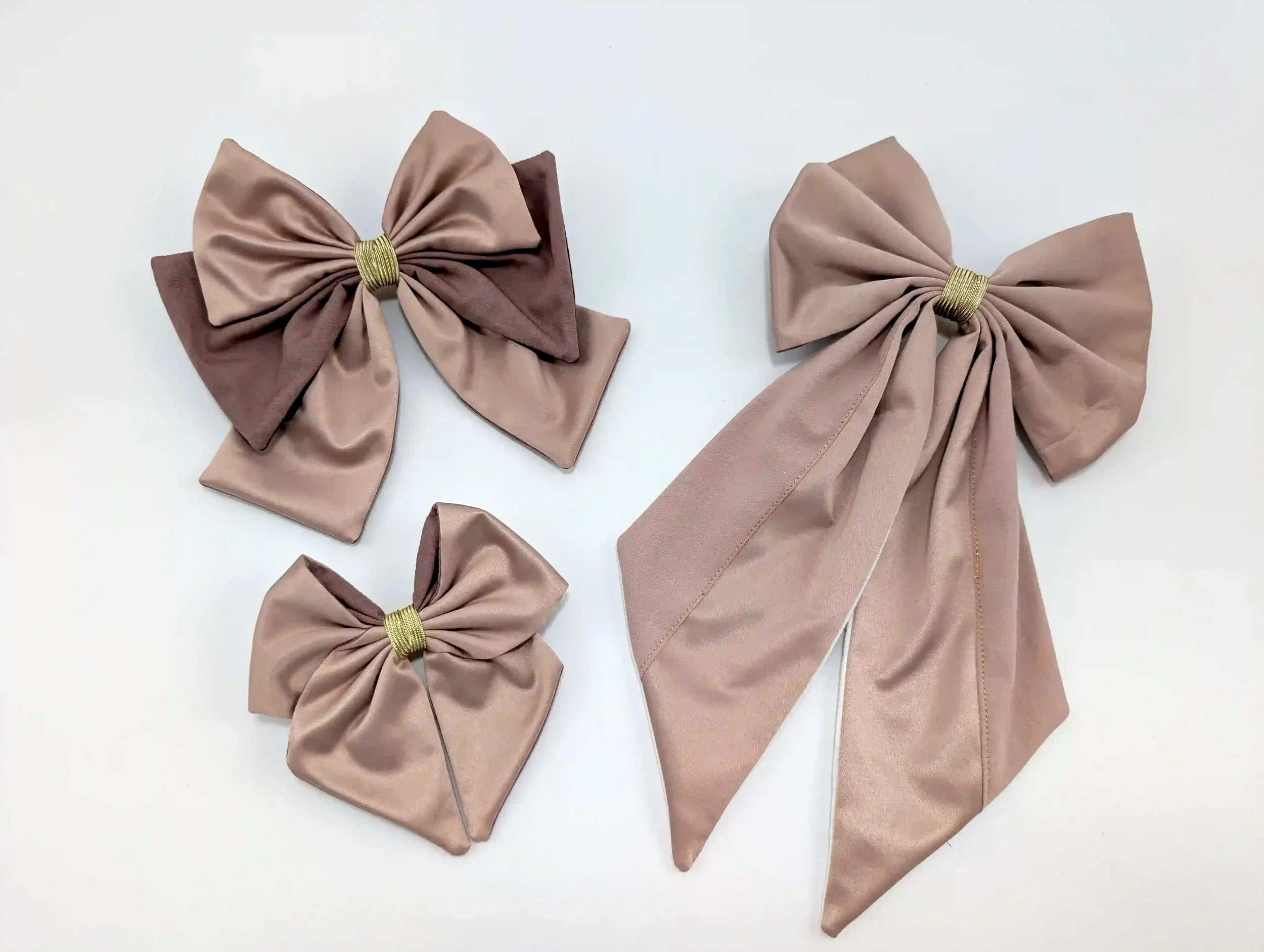 Quatre nœuds pour cheveux rose poudré de différentes tailles, avec détails dorés, présentés sur fond clair.