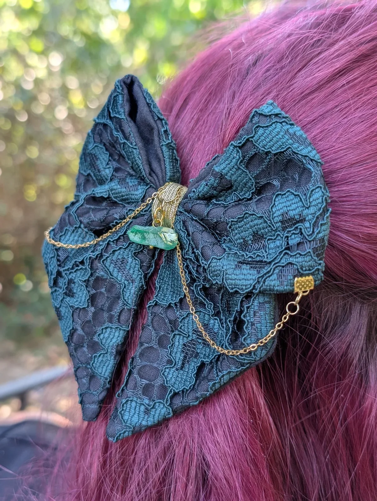 Noeud bijou vert bleuté en dentelle sur cheveux roses, chaînes dorées et cristal vert.
