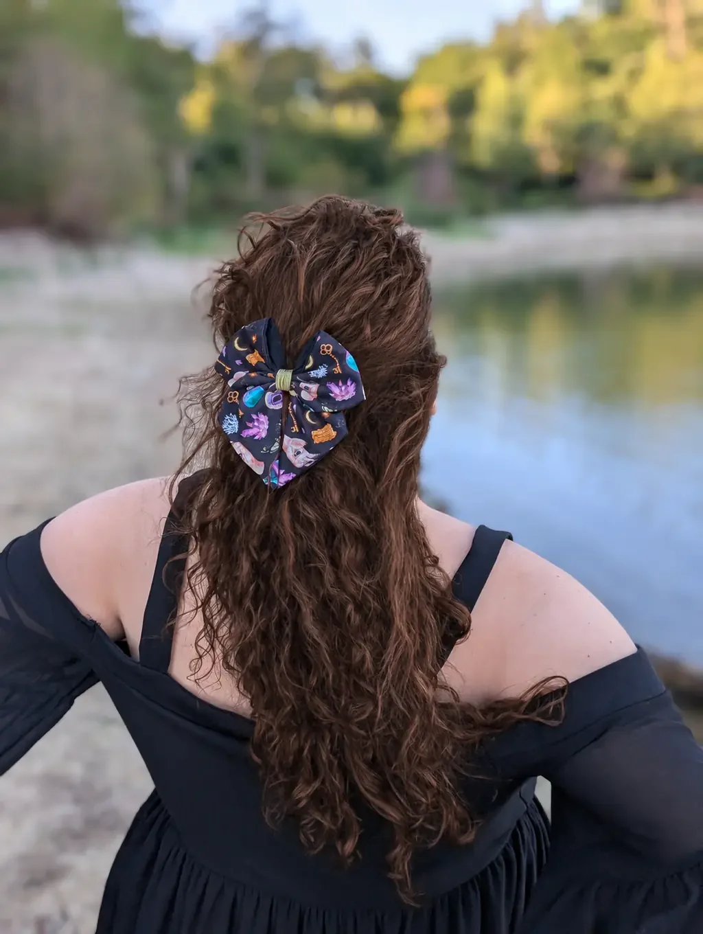 Petit nœud barrette Clés d’Arcane noir à cristaux violets porté sur cheveux bruns au bord d’un lac.