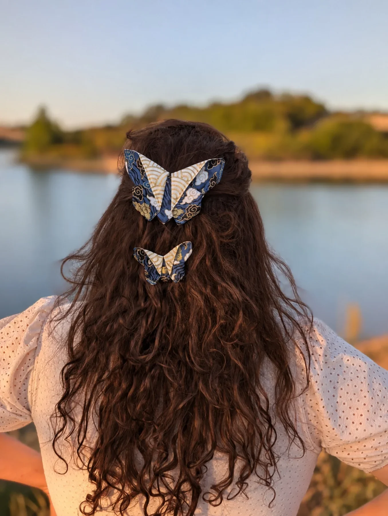 Deux barrettes papillon origami bleues et dorées dans des cheveux bruns vues de dos.
