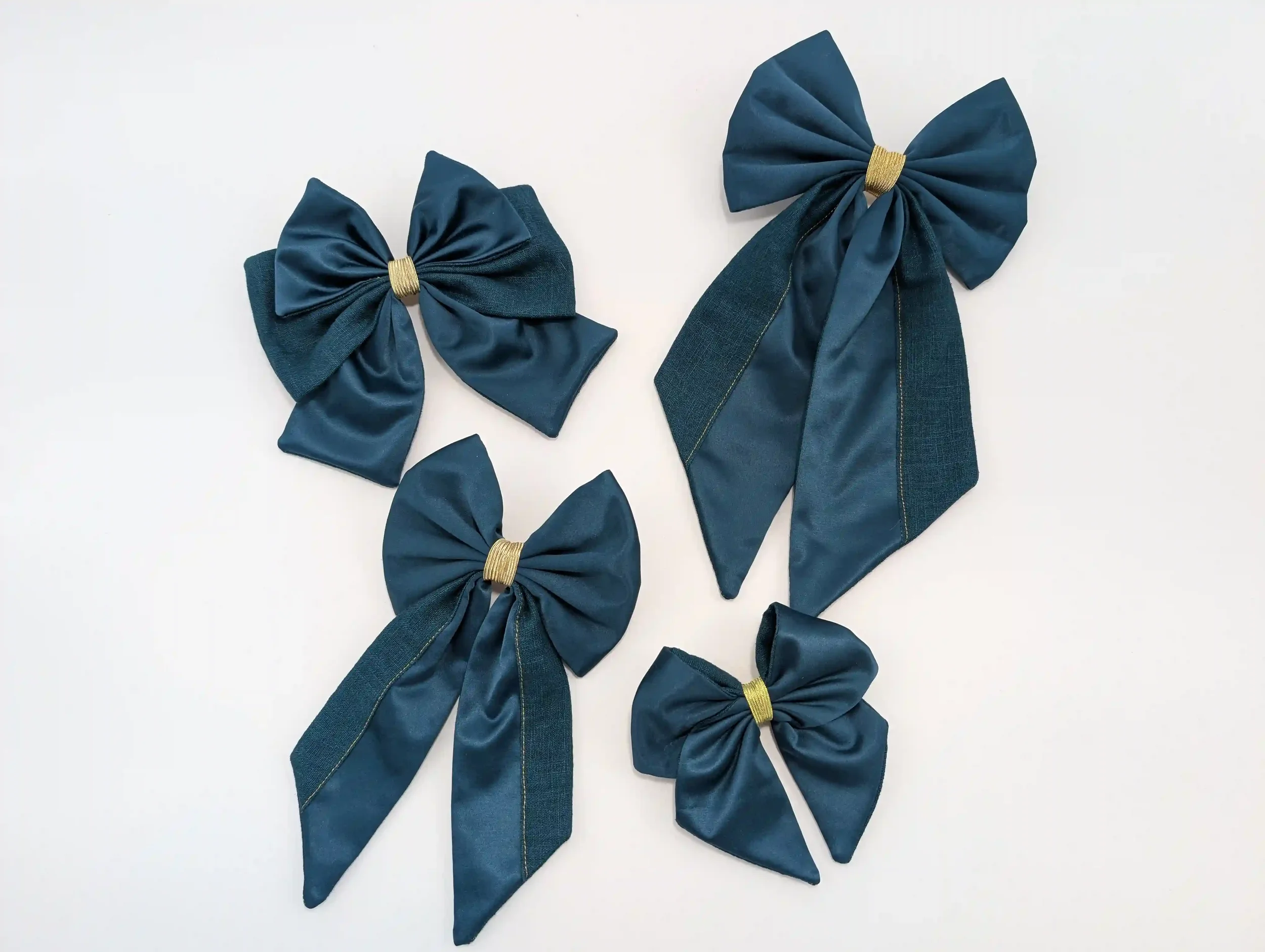 Quatre barrettes nœuds pour cheveux bleu pétrole de différentes tailles, avec détails dorés.