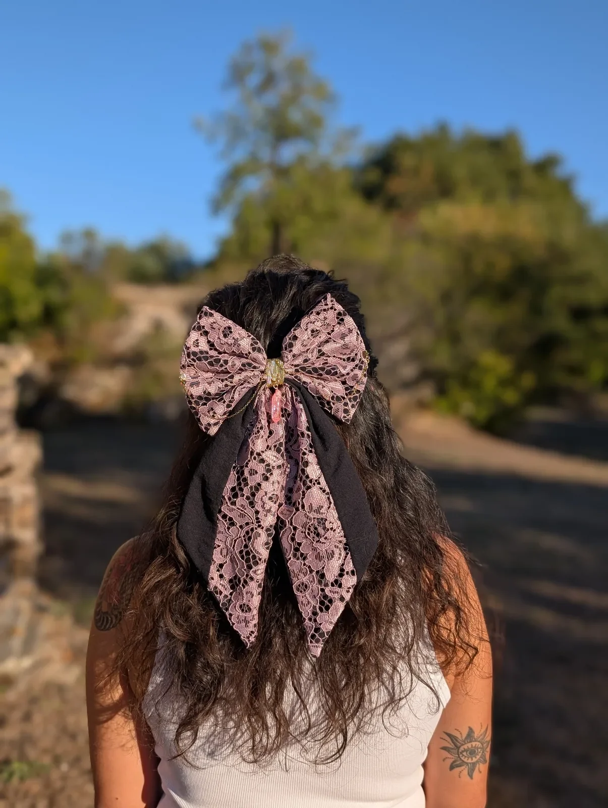 Noeud bijou en dentelle rose poudré à longues pointes noires, porté sur cheveux bruns.