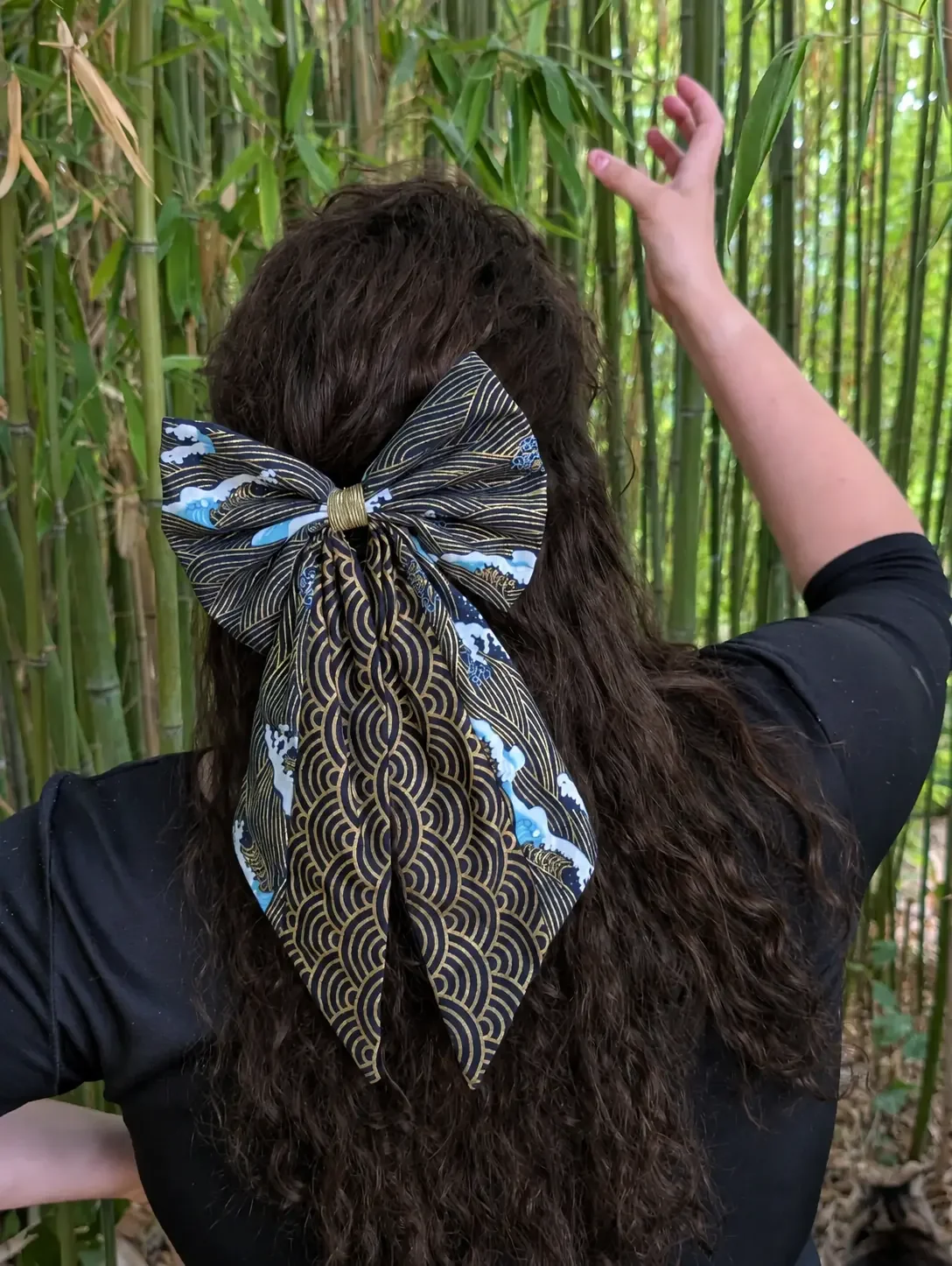 Nœud pour cheveux Nami to Awa noir, bleu et doré porté sur cheveux longs, dans un décor de bambous.