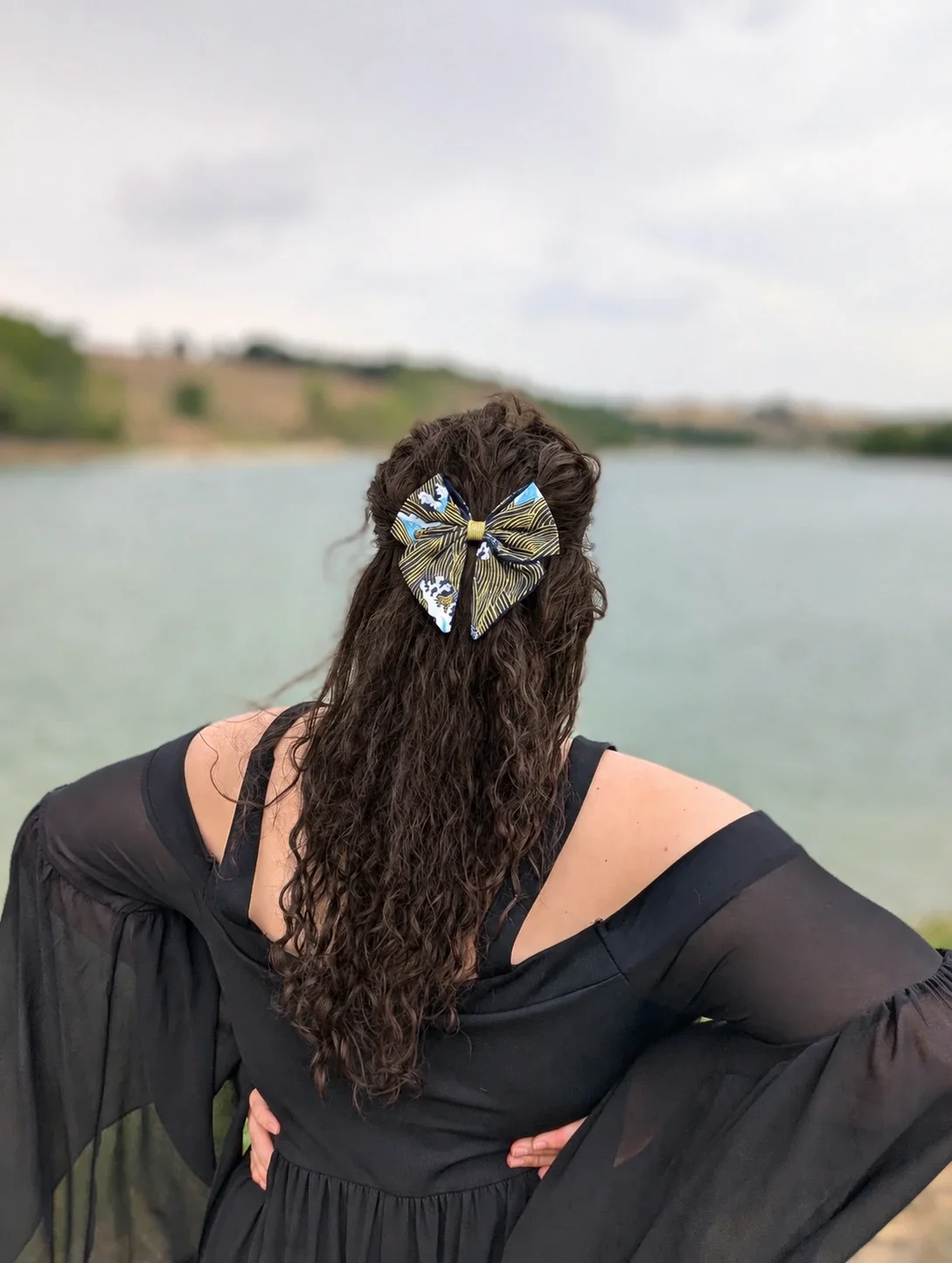 Grand noeud barrette Nami to Awa noir et or porté sur une coiffure semi-attachée au bord de l’eau.