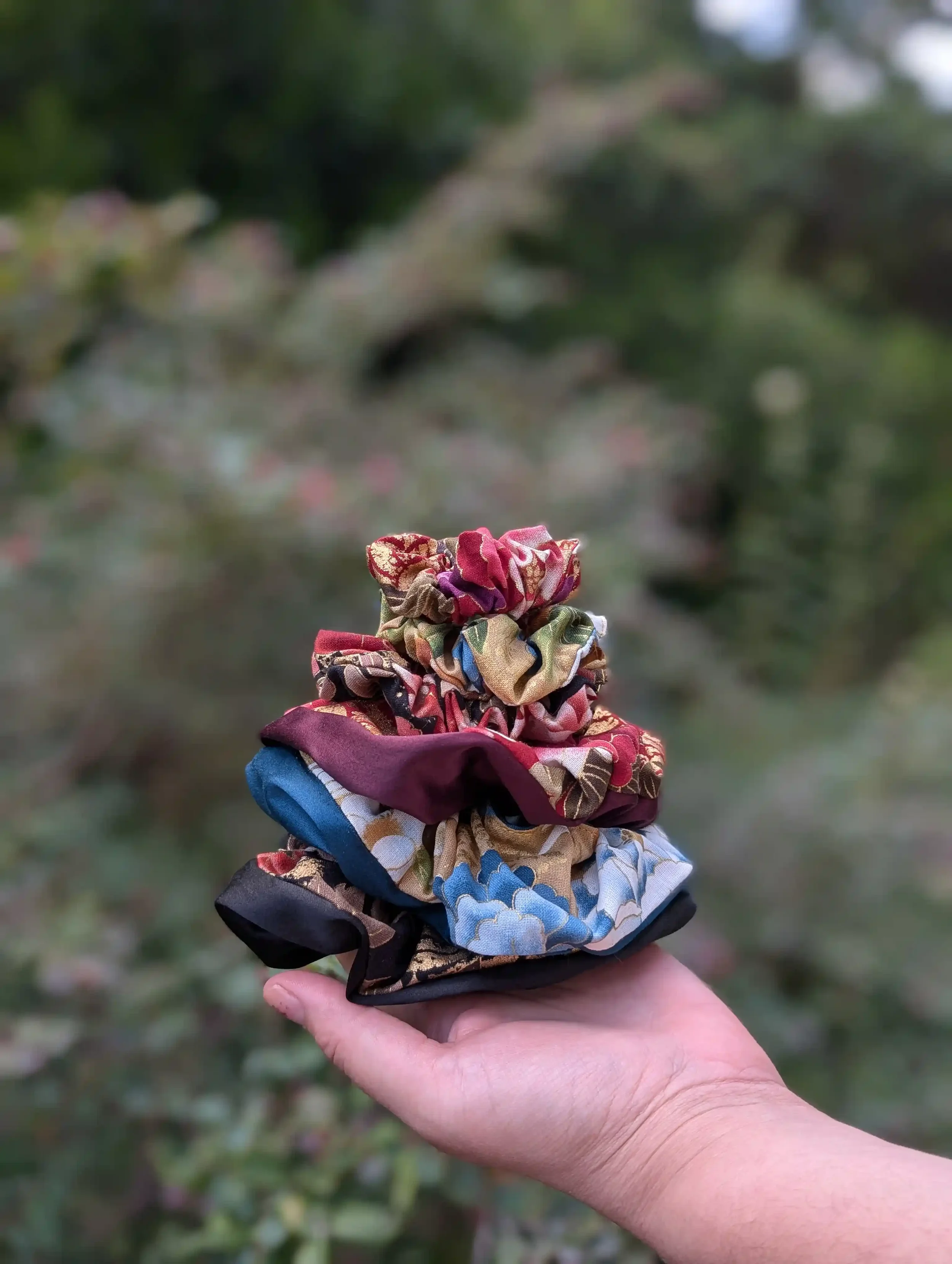 Collection de petits chouchous cheveux Tsuru en main, motifs floraux japonais dans plusieurs coloris, satin noir, bordeaux et bleu pétrole.