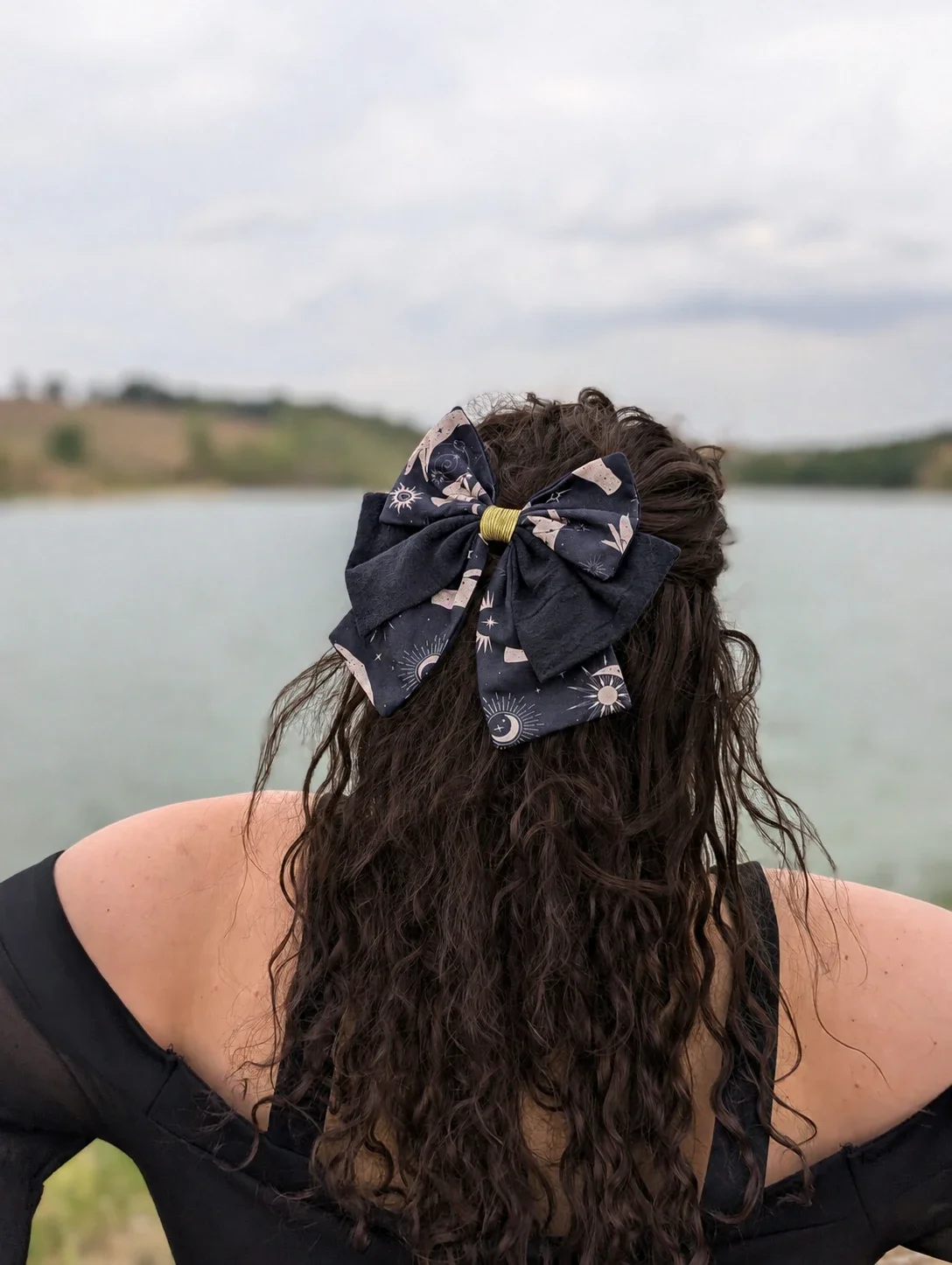 Noeud barrette Oracle Nocturne noir à motifs célestes et coton lavé, porté sur des cheveux longs bouclés.