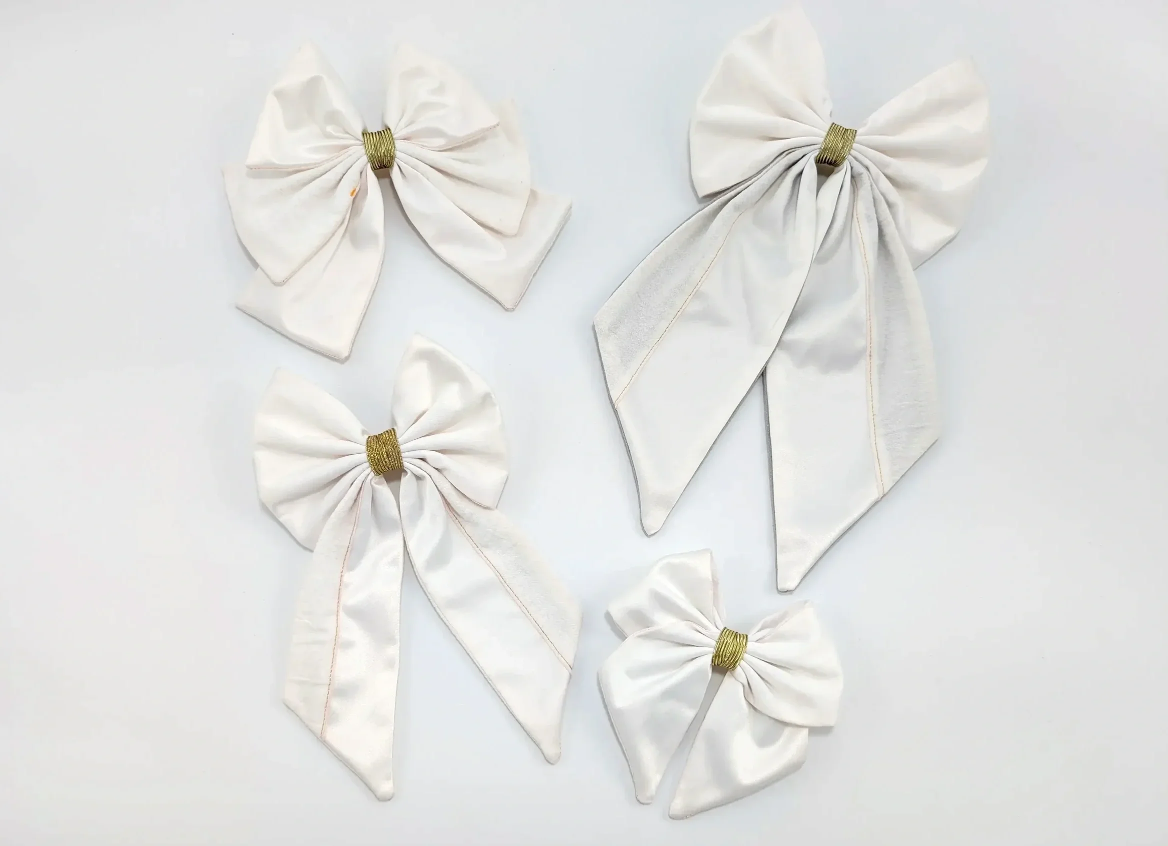 Quatre nœuds pour cheveux blancs de différentes tailles, avec détails dorés, présentés sur fond clair.