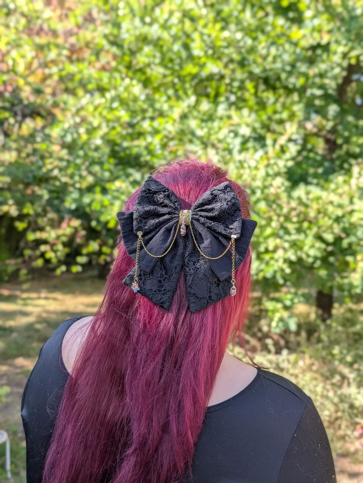 Nœud bijou en dentelle noire porté sur cheveux roses, chaînes dorées et deux étoiles en verre teinté.