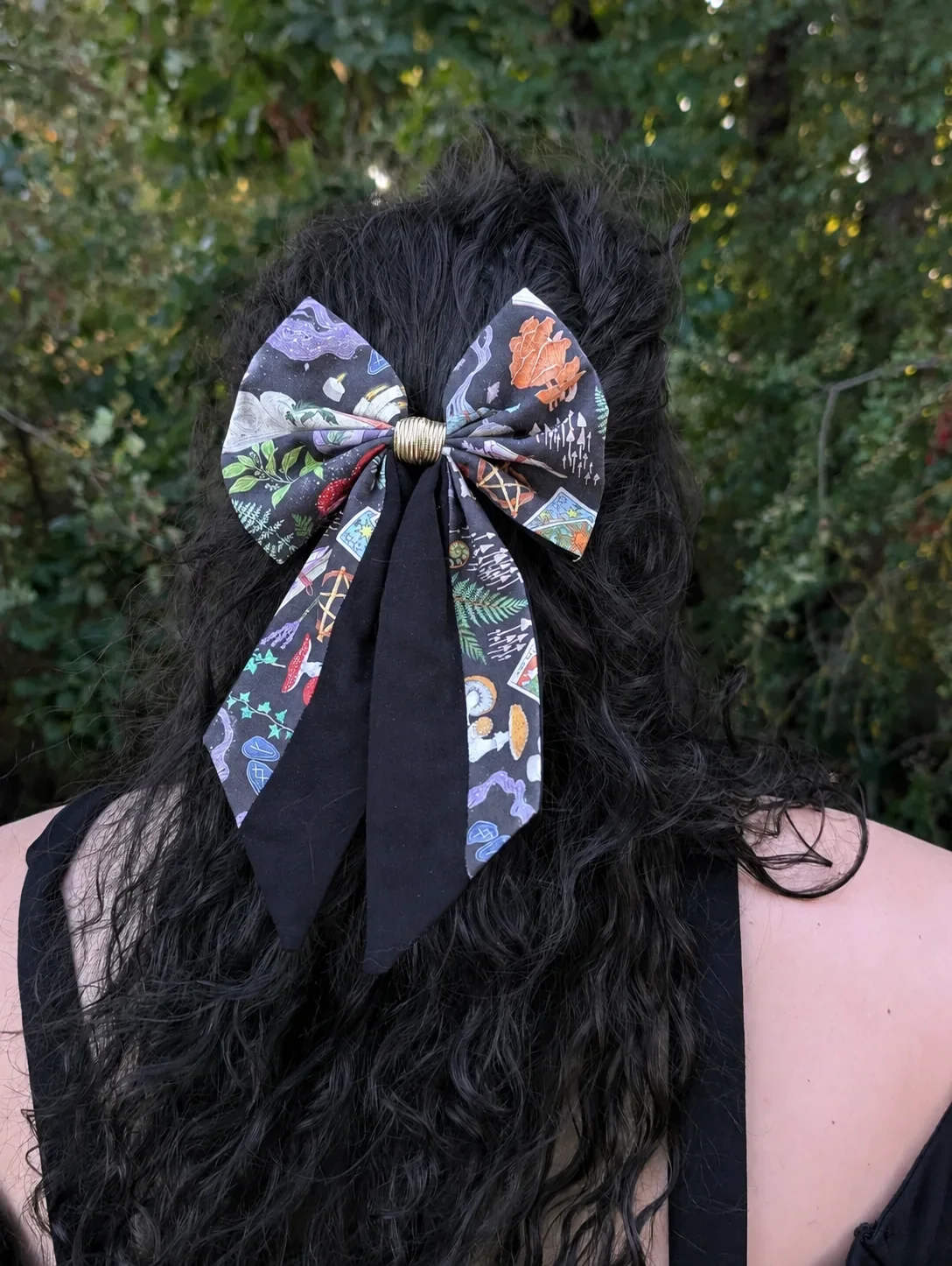 Nœud barrette Grimoire des bois à longues pointes noires et imprimées, porté sur cheveux noirs bouclés.
