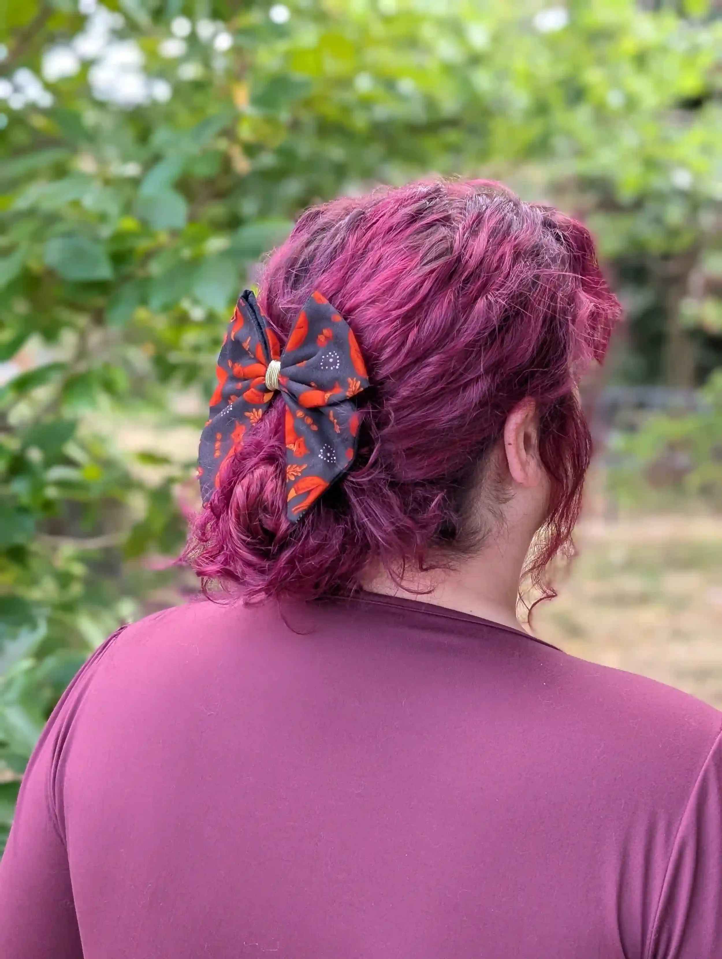Nœud cheveux Renards porté sur un chignon bas, vue rapprochée, motif de petits renards roux et feuillages sur fond noir.