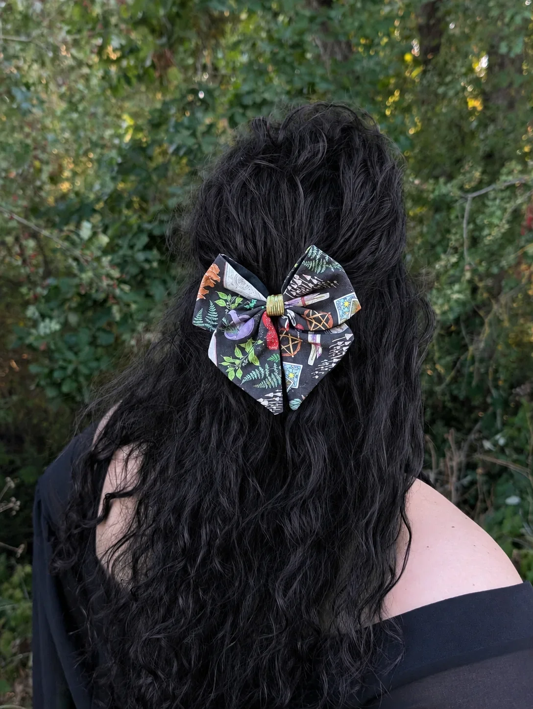 Noeud Grimoire des bois à motifs féeriques porté en demi-queue sur de longs cheveux noirs bouclés.