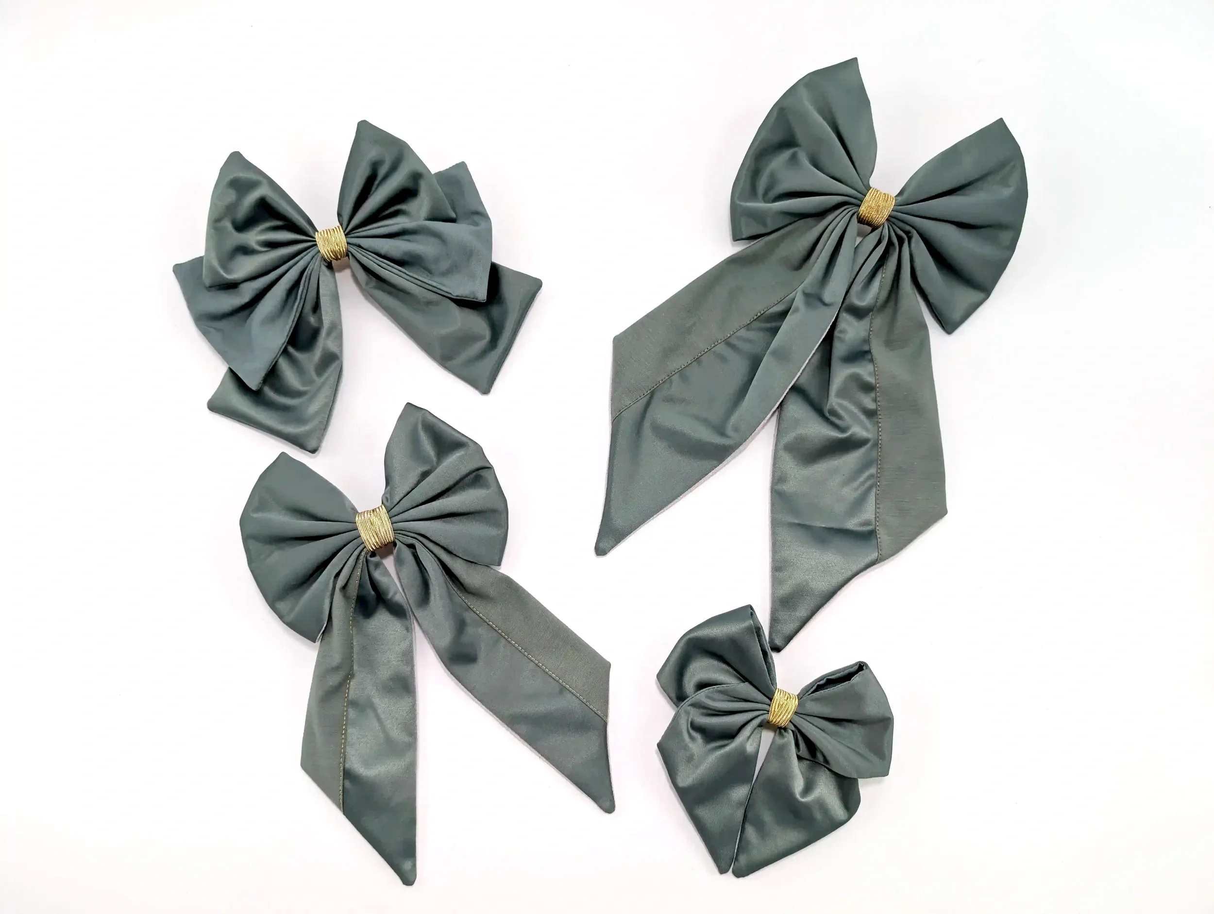 Quatre barrettes nœuds pour cheveux gris vert de différentes tailles, avec finitions dorées.