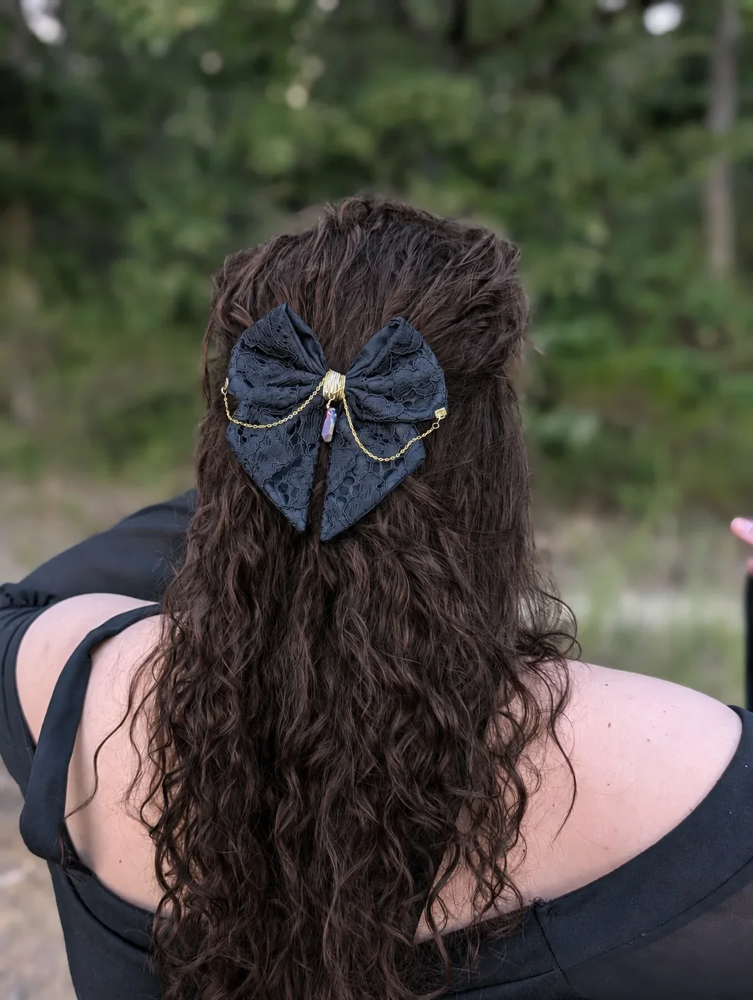 Noeud bijou en dentelle noire sur cheveux bruns bouclés, vue de dos en extérieur.