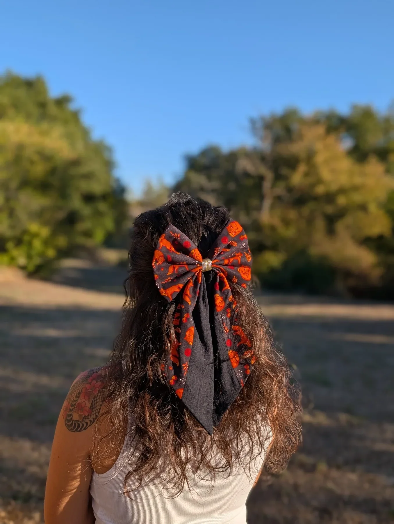 Nœud barrette Renard noir et orange à longs pans porté en demi-queue sur cheveux bruns bouclés.