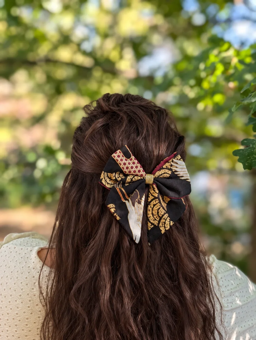 Petit noeud Ailes de grue noir a motif de plumes blanches sur cheveux bruns.