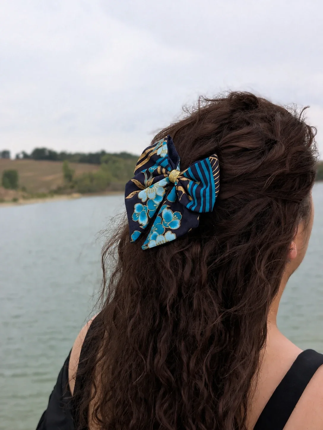 Petit nœud pour cheveux Hana to Nami bleu marine, turquoise et or porté sur une demi-queue, vue de côté.