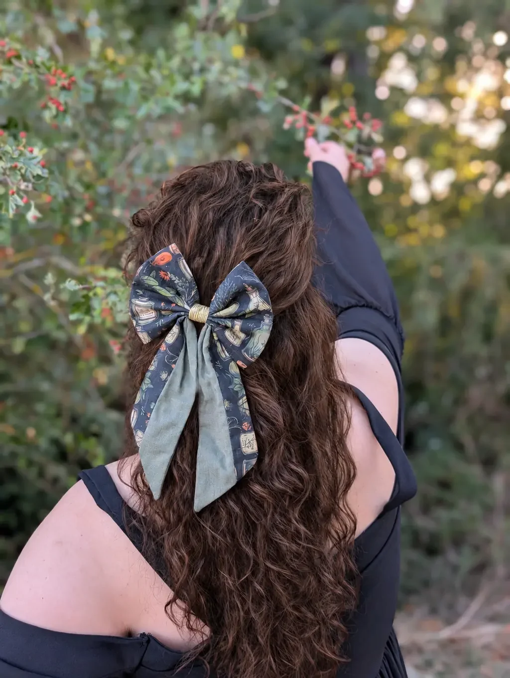 Nœud barrette Alchimique à motifs de fioles et de plantes avec longs pans vert sauge porté sur cheveux bruns bouclés.