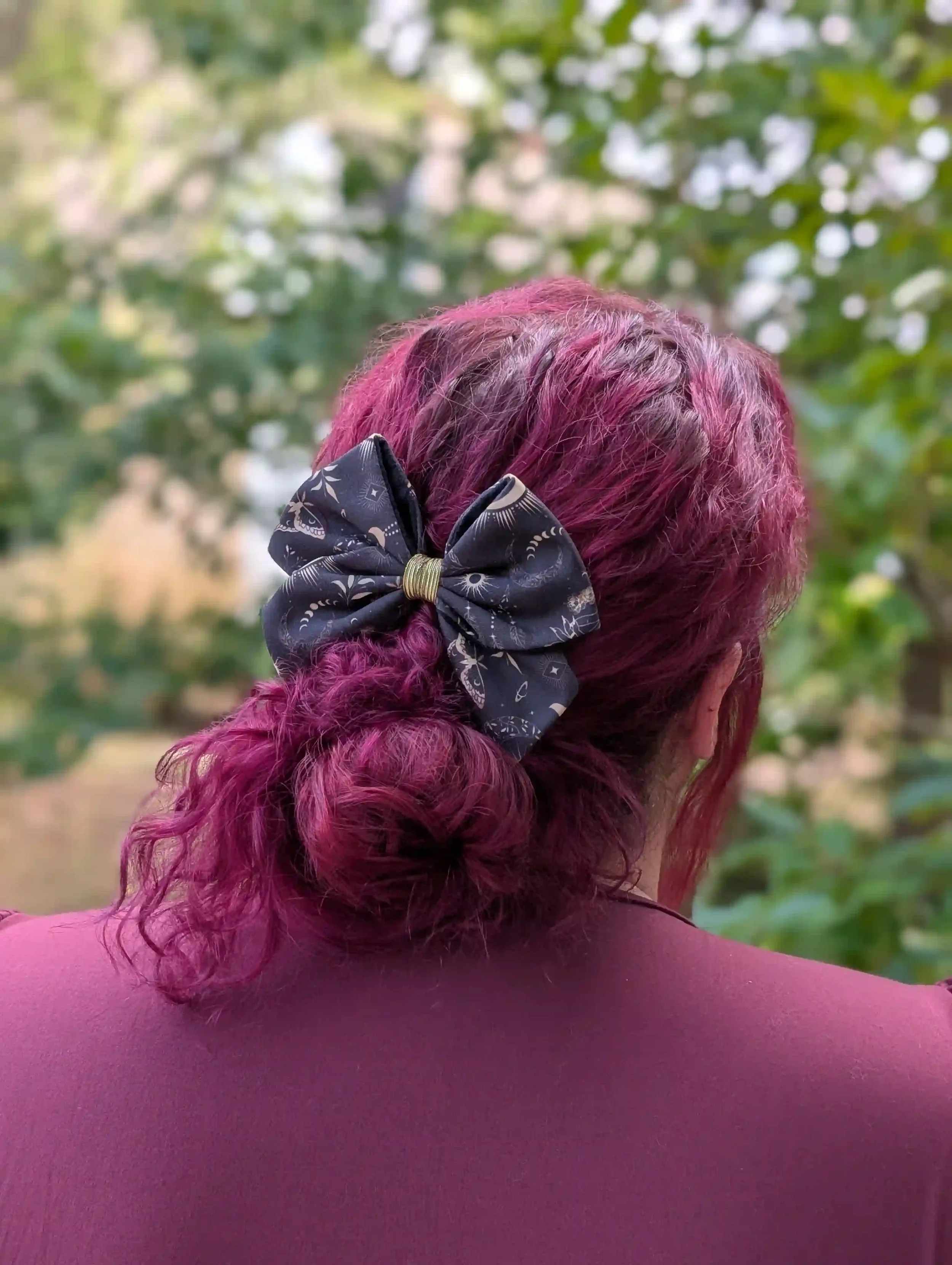 Nœud cheveux Moon porté sur un chignon bas, vue de dos, motifs de lunes et main mystérieuse sur fond sombre.
