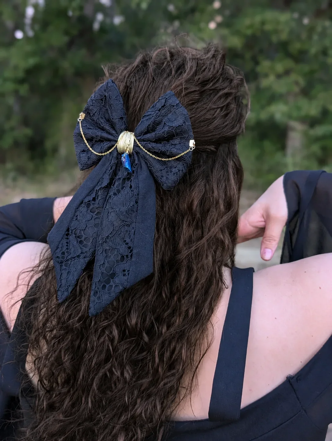 Noeud bijou noir en dentelle à longues pointes, porté sur cheveux bruns bouclés.