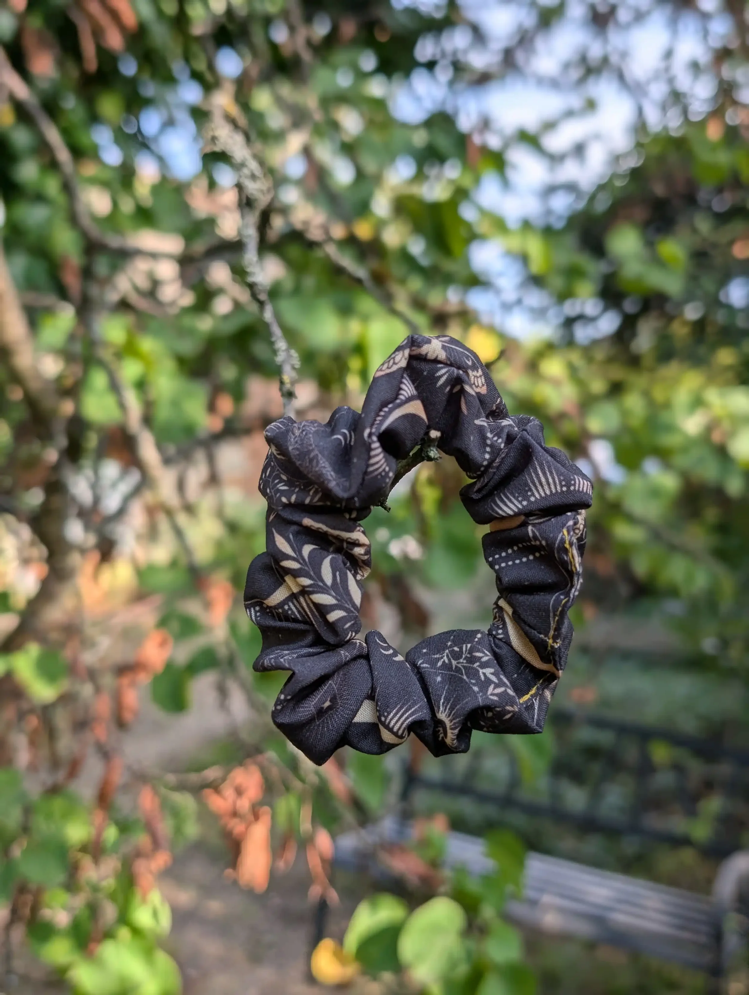 Petit chouchou Dark Moon noir et doré suspendu à une branche, motifs de lunes et détails célestes