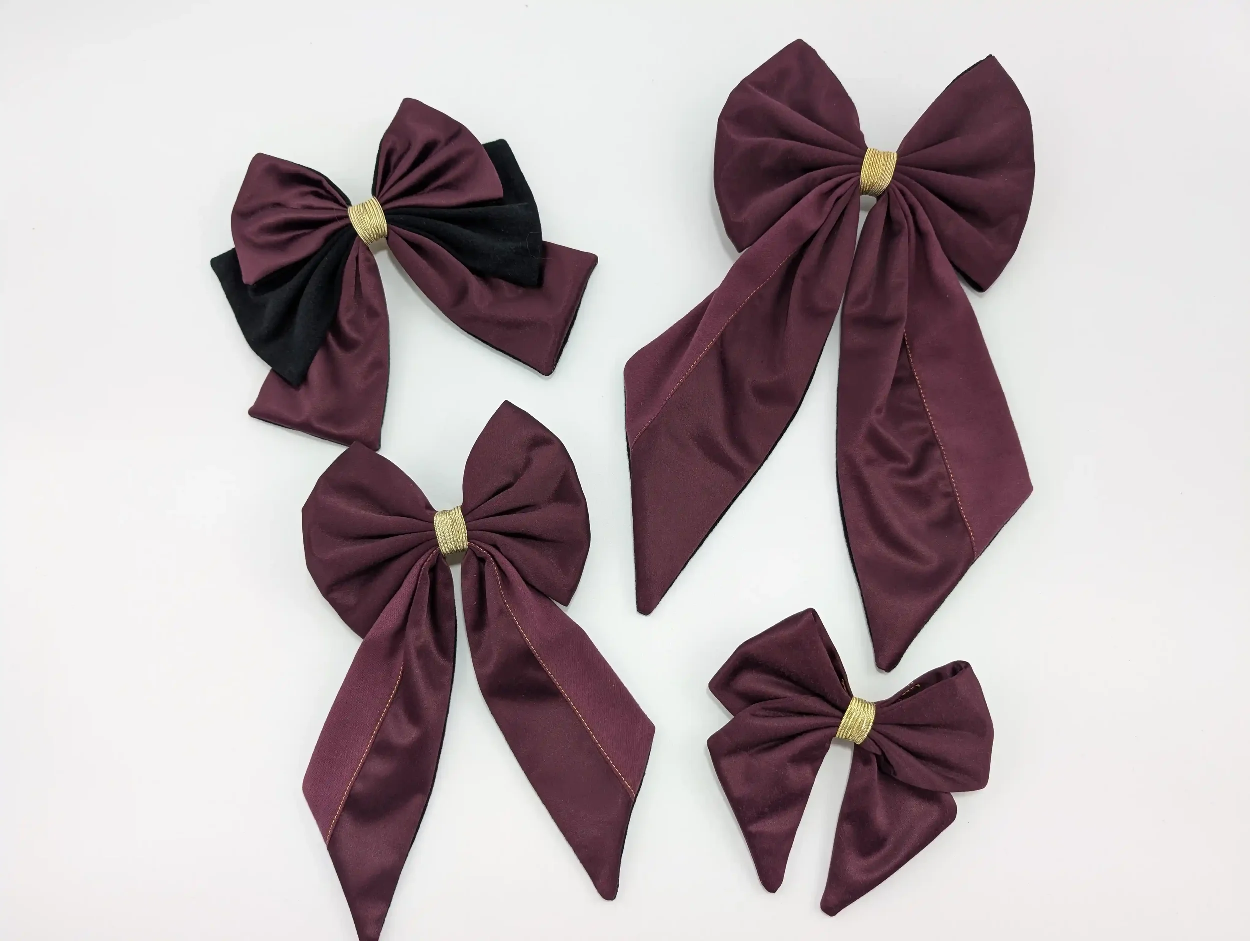 Quatre barrettes nœuds pour cheveux bordeaux foncé de différentes tailles, avec détails dorés.