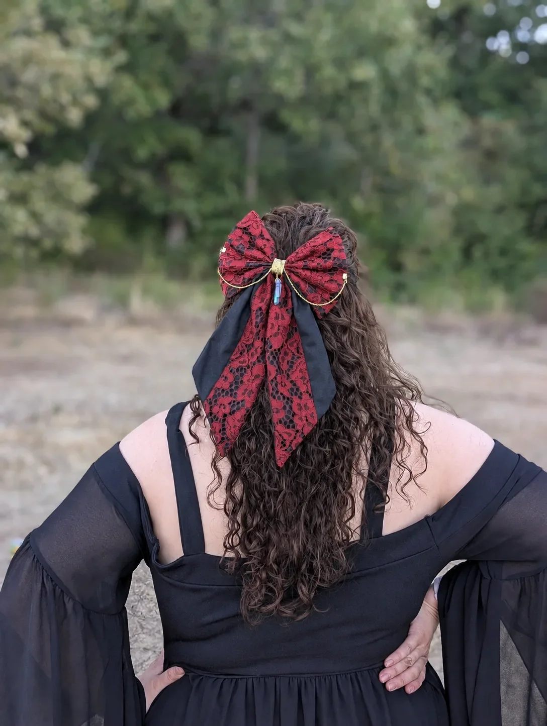 Noeud bijou rouge et noir à longues pointes porté sur cheveux bruns bouclés, vu de dos.