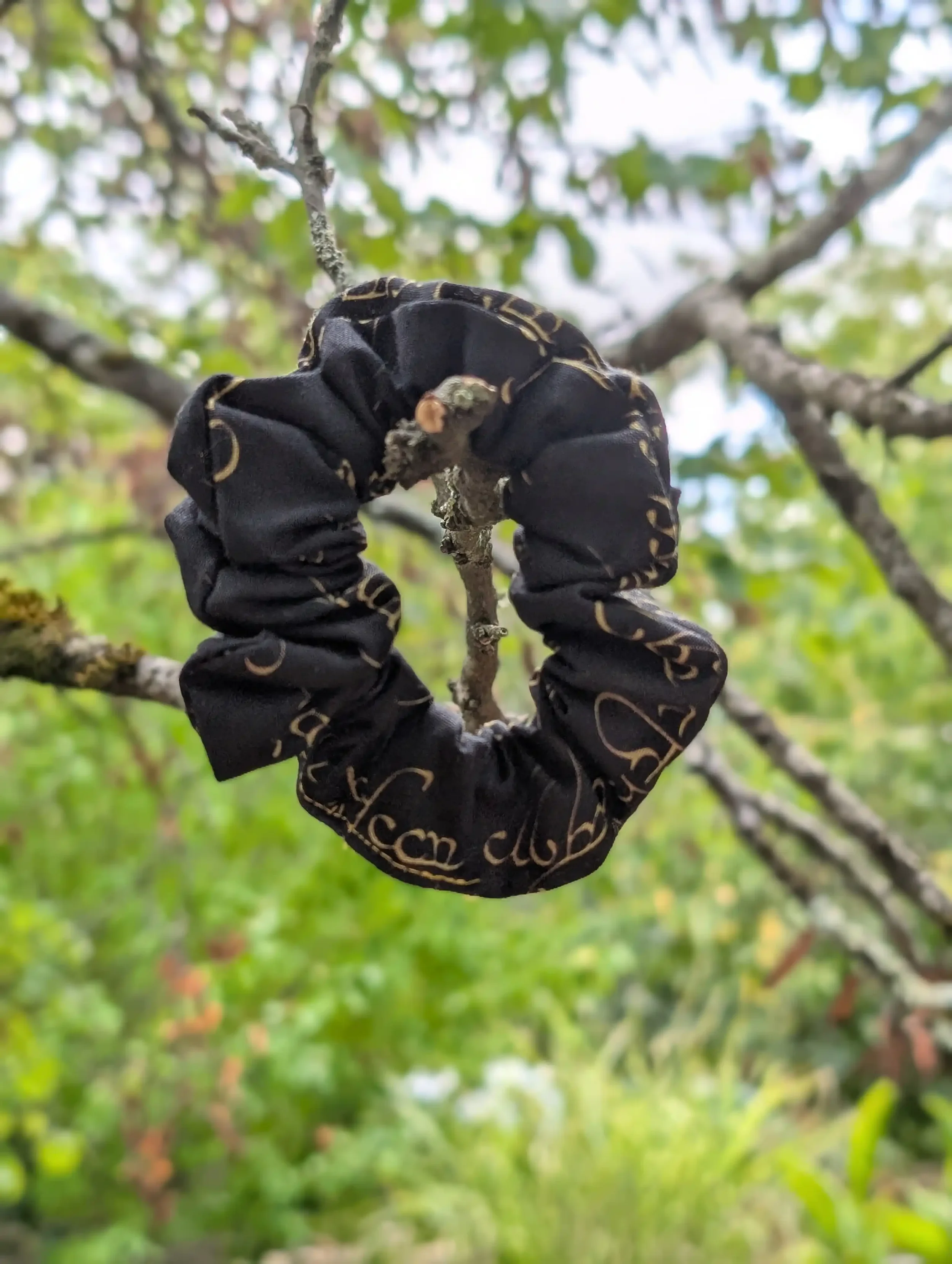 Petit chouchou Elfique noir et or suspendu à une branche, tissu imprimé à écriture dorée