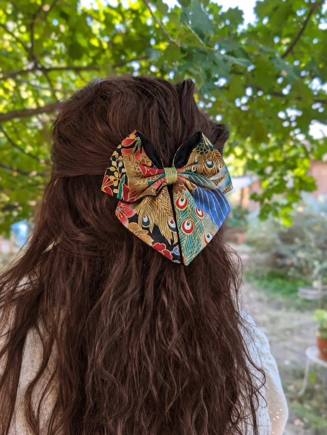 Petit noeud japonais Plumes de paon colorees porte sur cheveux bruns.