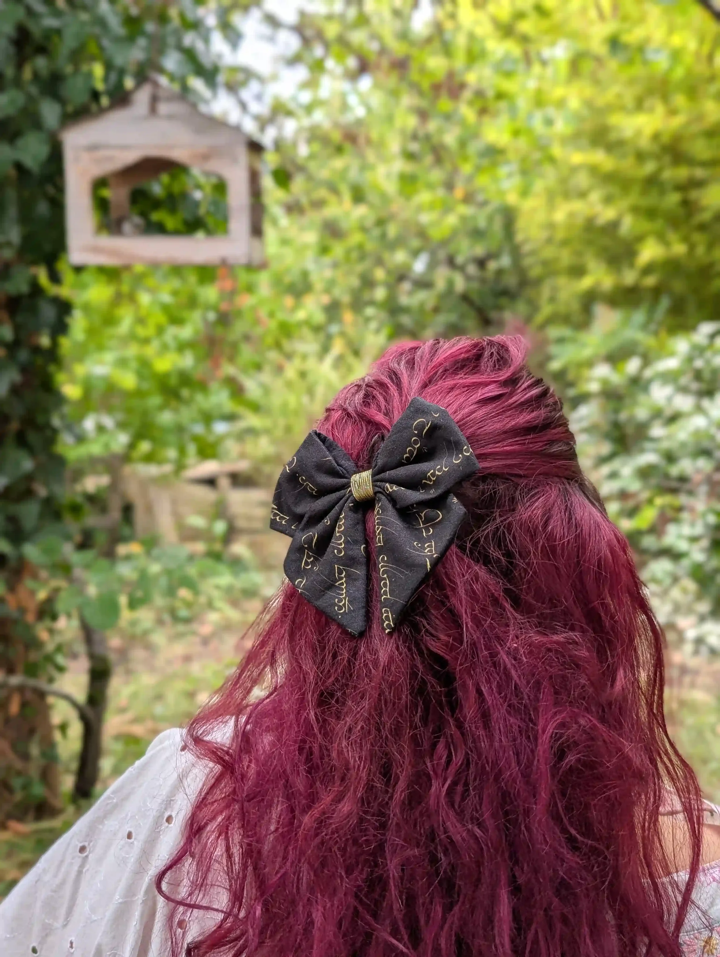 Nœud cheveux Elfique porté en demi-queue dans un jardin, écriture mystique dorée sur fond noir.