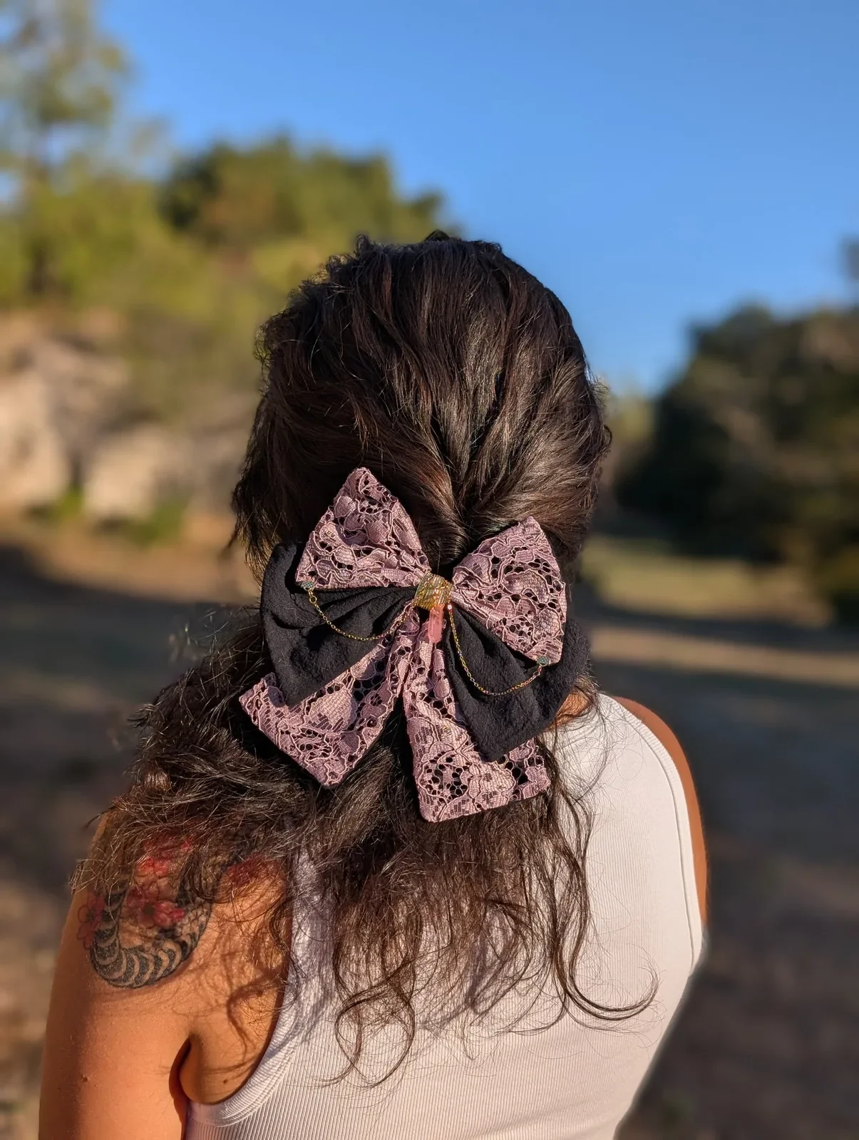 Noeud bijou rose poudré en dentelle et chaînes dorées, porté en demi-queue de dos.