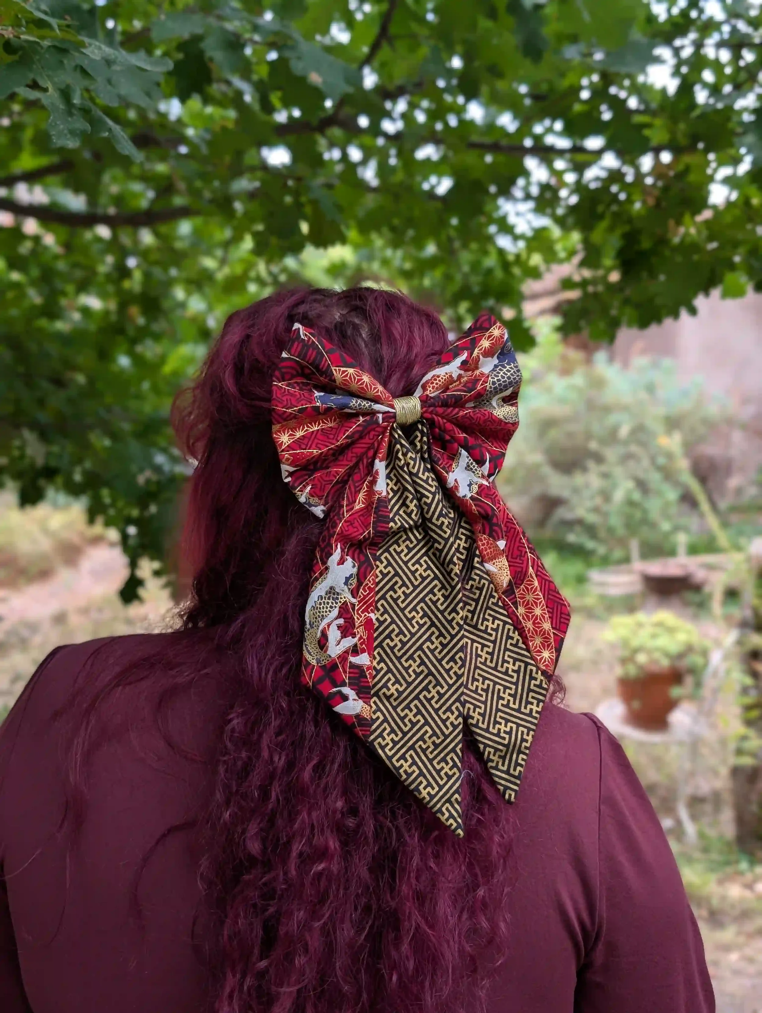 Nœud cheveux Koï rouge porté en demi-queue, vue de dos sous un arbre, motif carpes japonaises dorées sur tissu Sayagata bordeaux et or.