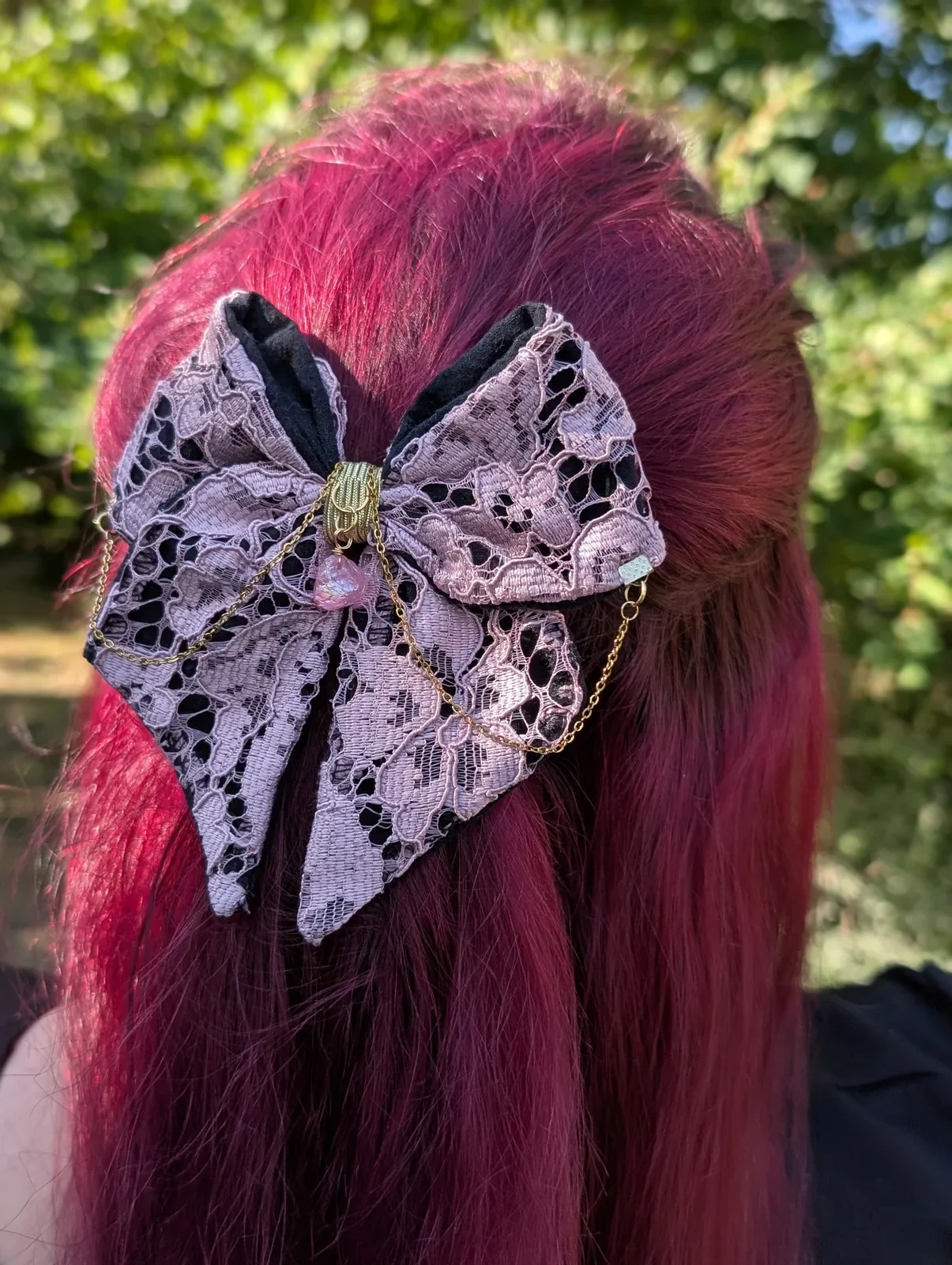 Nœud bijou en dentelle rose sur cheveux roses, chaînes dorées et cristal rose, vue rapprochée.