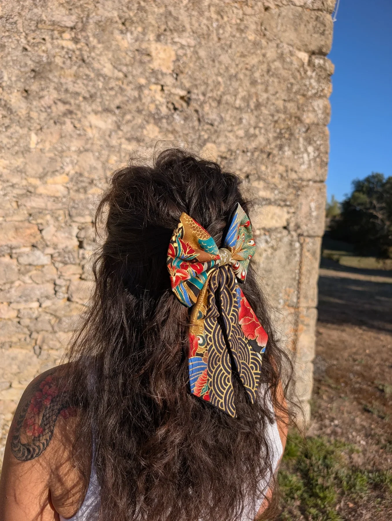Grand noeud Plumes de paon avec longs pans bleu rouge et or vu de cote.