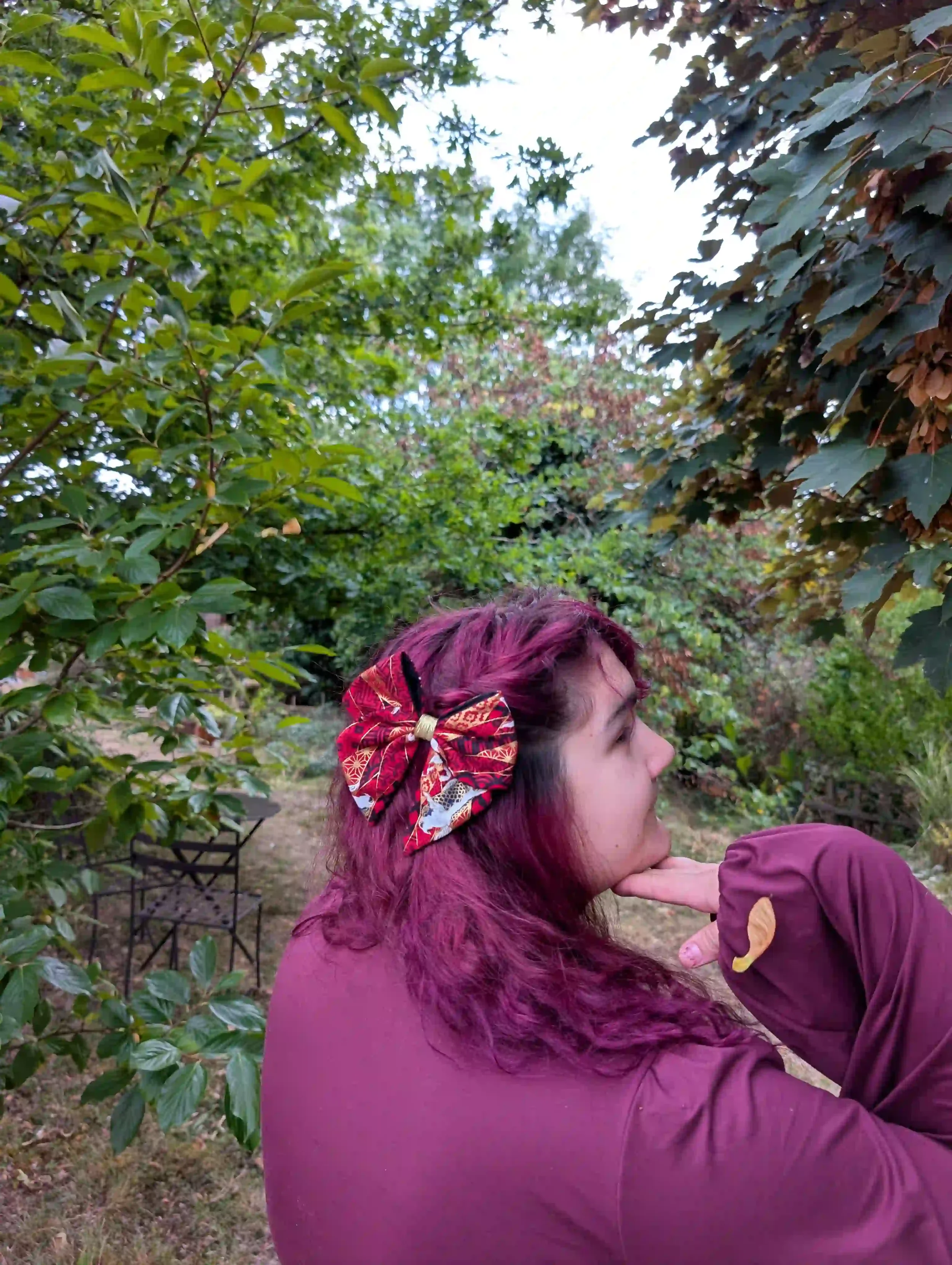 Nœud cheveux Koï rouge taille S porté en demi-queue, vue de profil dans un jardin, motif carpes japonaises dorées sur tissu Sayagata bordeaux et or.