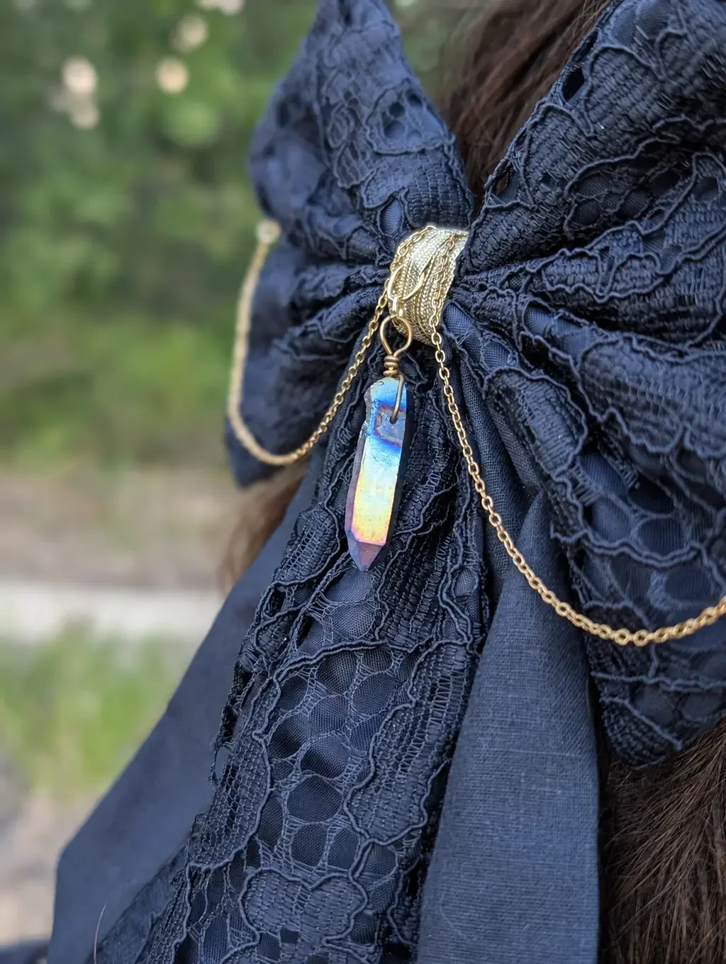 Nœud bijou noir en dentelle, chaînes dorées et cristal sur cheveux bruns, trés gros plan.