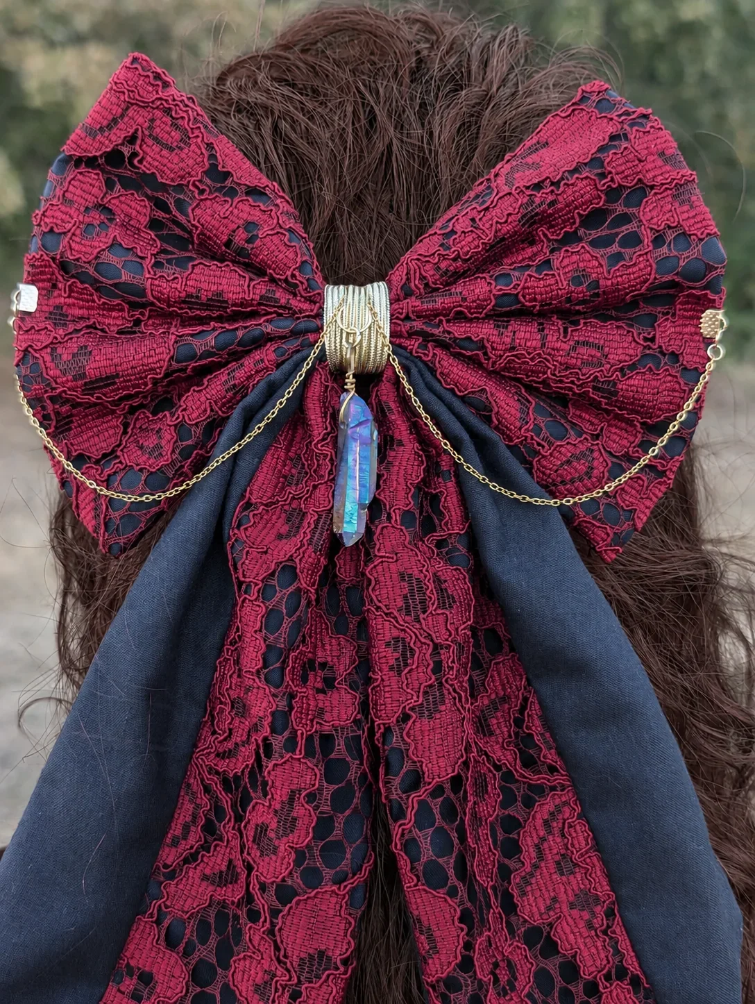 Nœud bijou en dentelle rouge sur fond noir, chaînes dorées et cristal bleu, détail de dos.