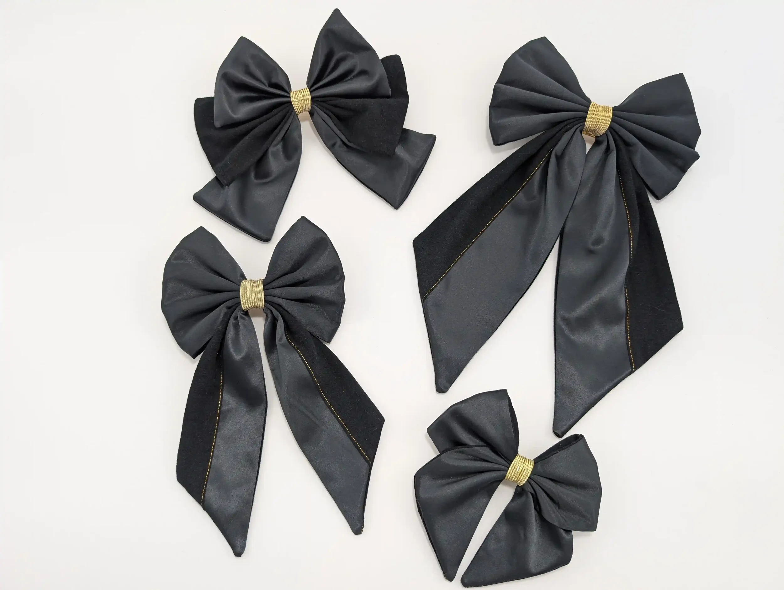 Quatre nœuds pour cheveux noirs de différentes tailles, avec finitions dorées et détails en tissu texturé.