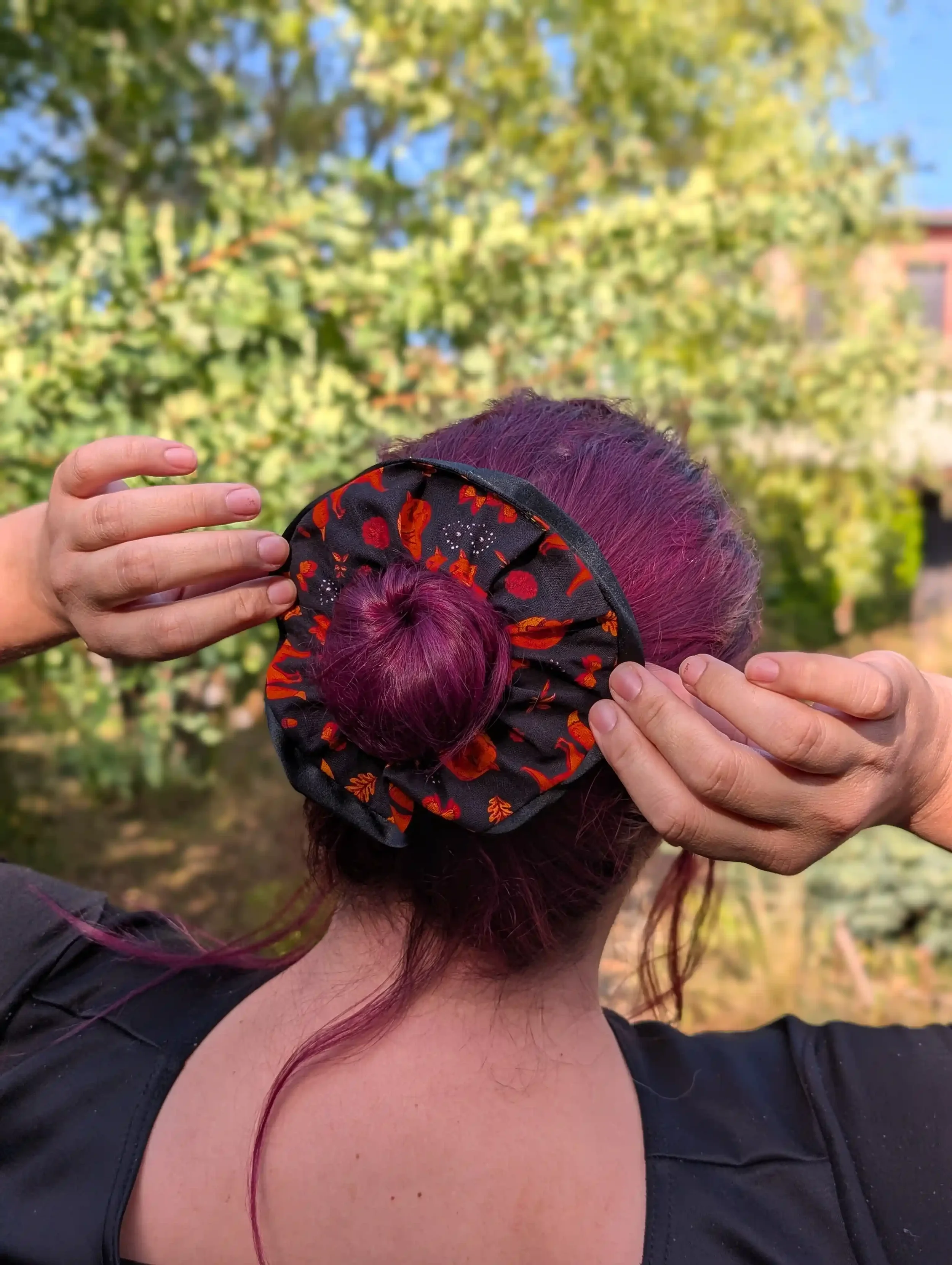 Grand chouchou Renards noir et rouille avec satin noir porté autour d’un chignon et tenu avec les mains