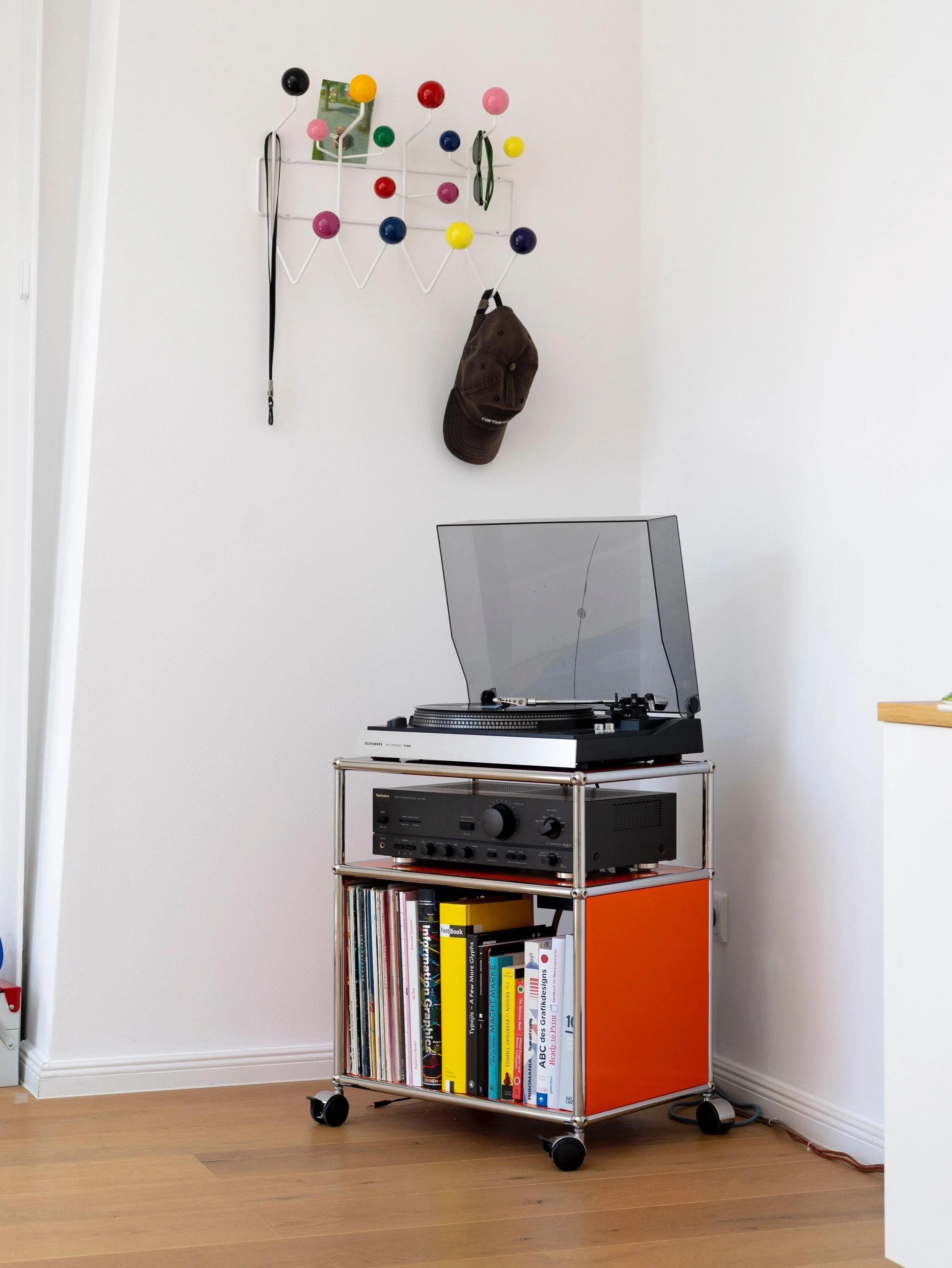 USM Lowboard in Orange mit Plattenspieler und Schallplattensammlung. An der Wand eine Garderobe mit bunten Kugeln von vitra