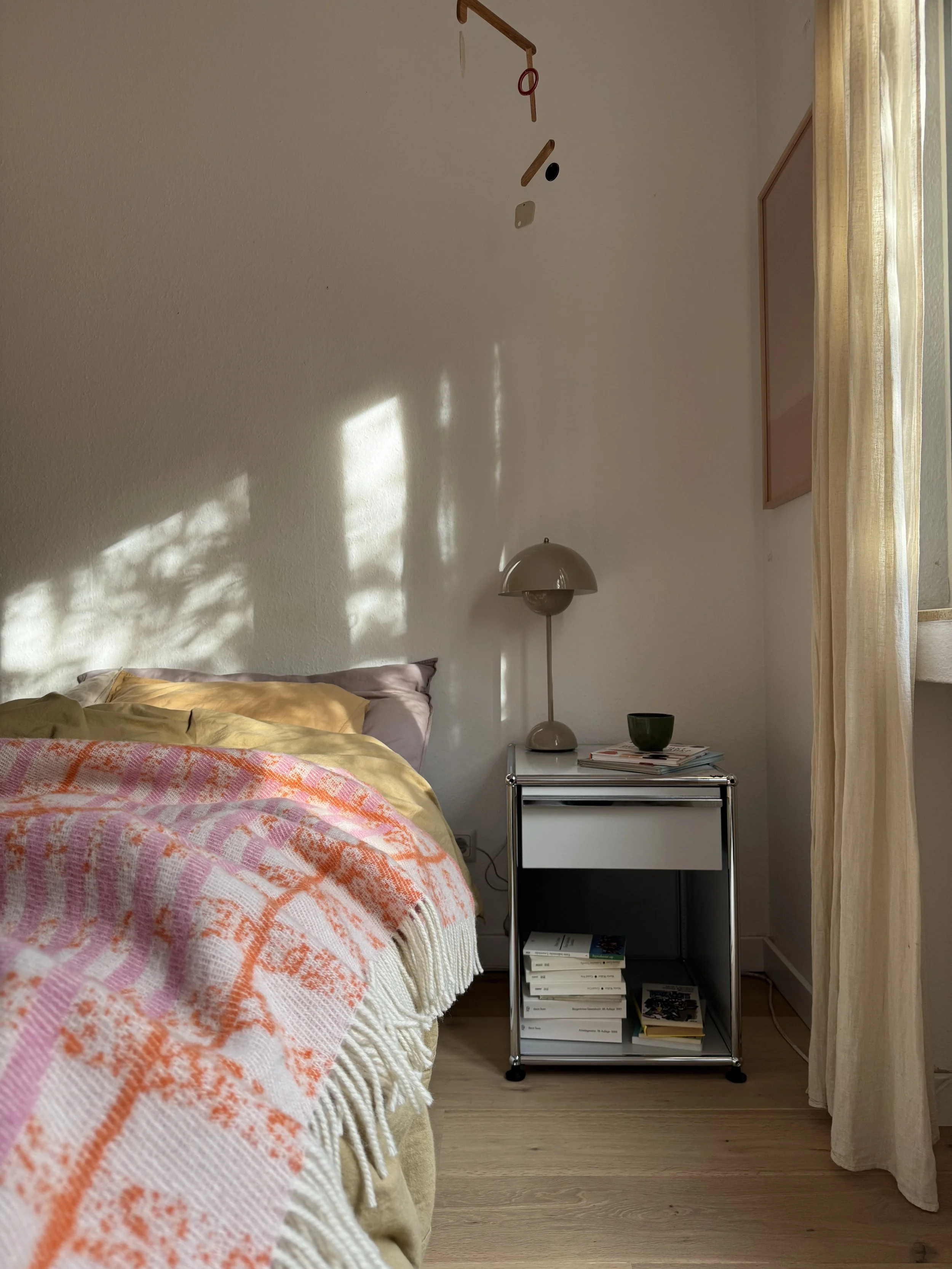 Schlafzimmer mit USM Nachttisch in grau, auf dem Bett eine bunte Tagesdecke