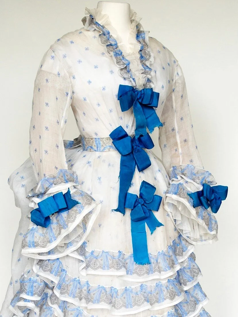 💙 The muslin has a printed &agrave; disposition design of blue bows on a black lace edging. The bodice is unlined so the camisole worn beneath can be seen through the sheer fabric.

Muslin dress, 1872-1876, maker unknown, The Hopkins Costume Trust
.