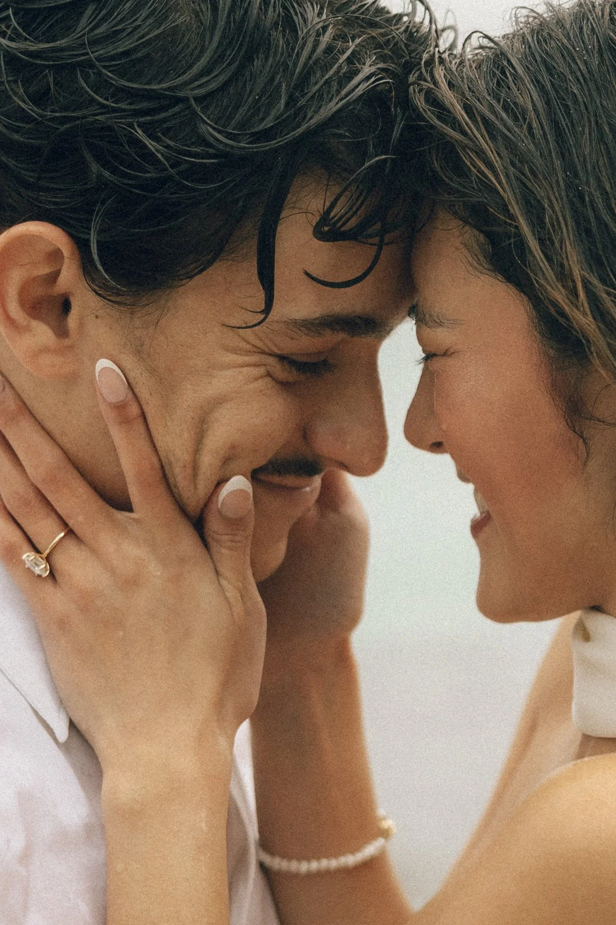 A close-up of two people touching foreheads and smiling, with their eyes closed, showing intimacy and affection.